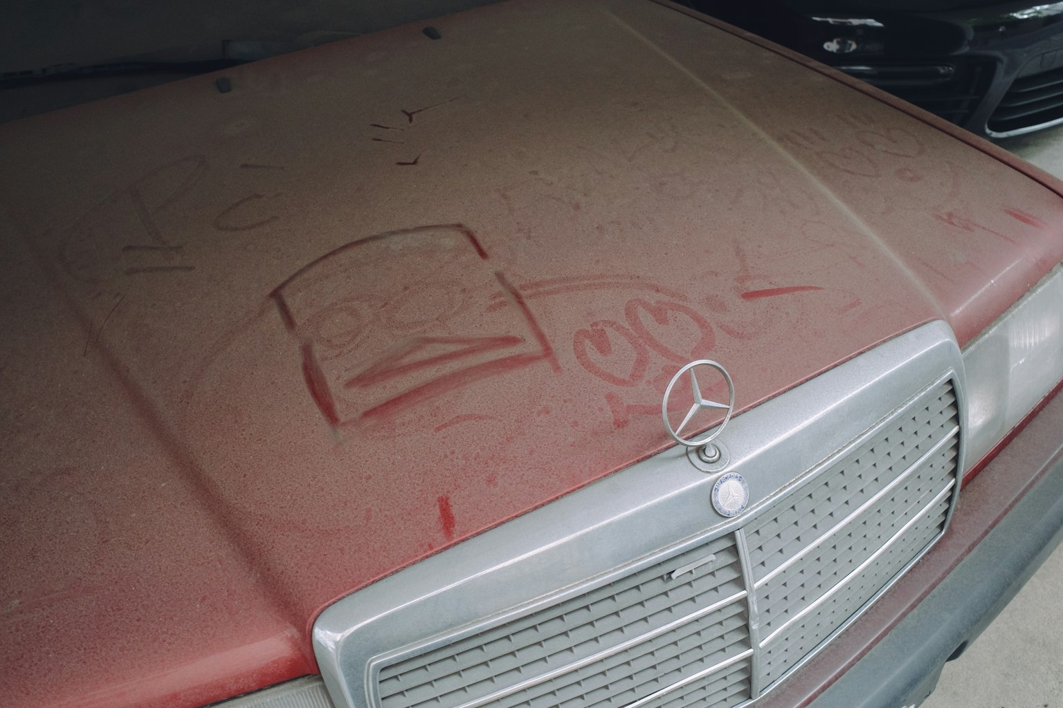 Capot de Mercedes recouvert de poussière avec des gribouillages