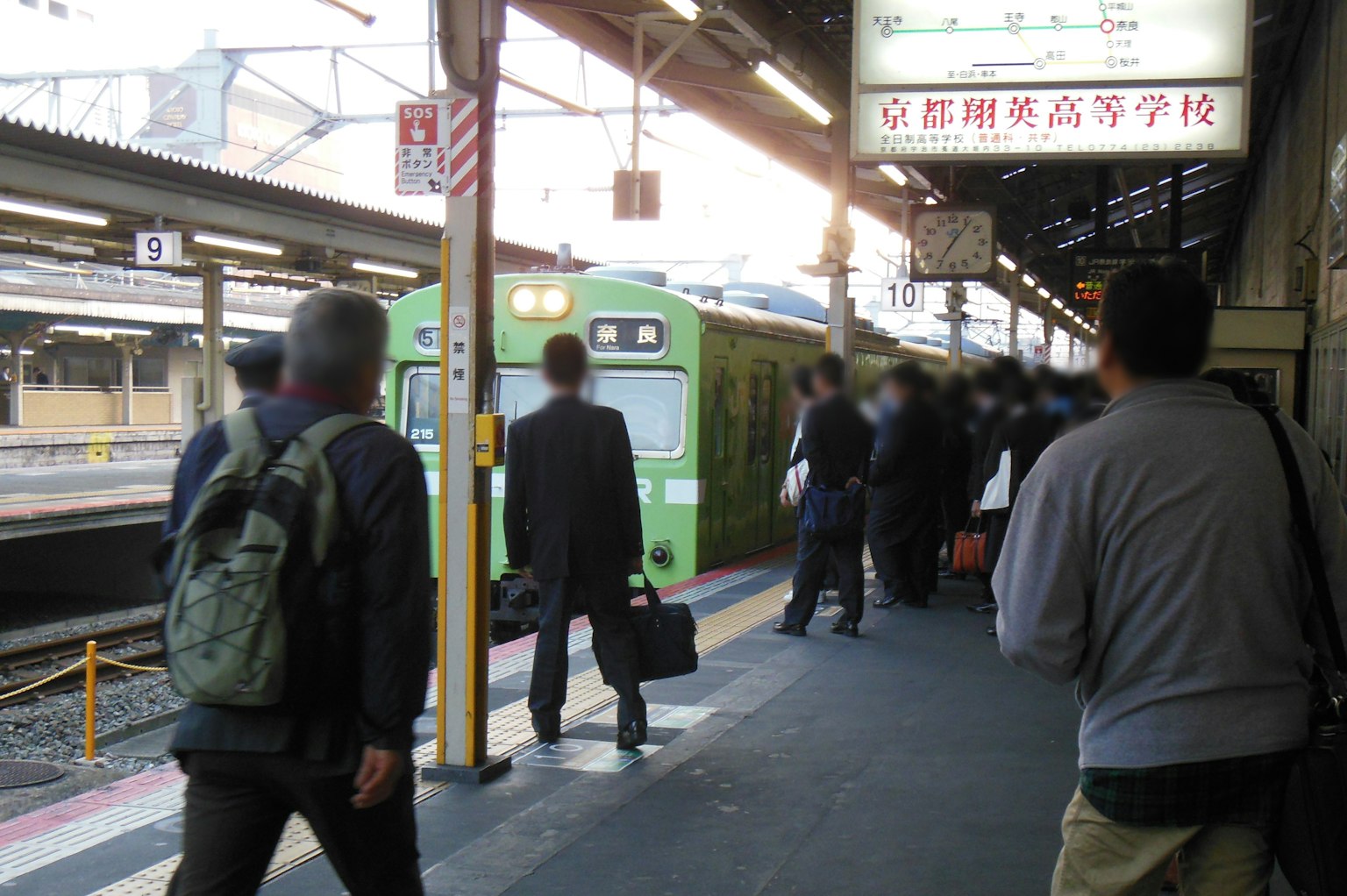 Passeggeri in attesa su una banchina con un treno verde alla stazione