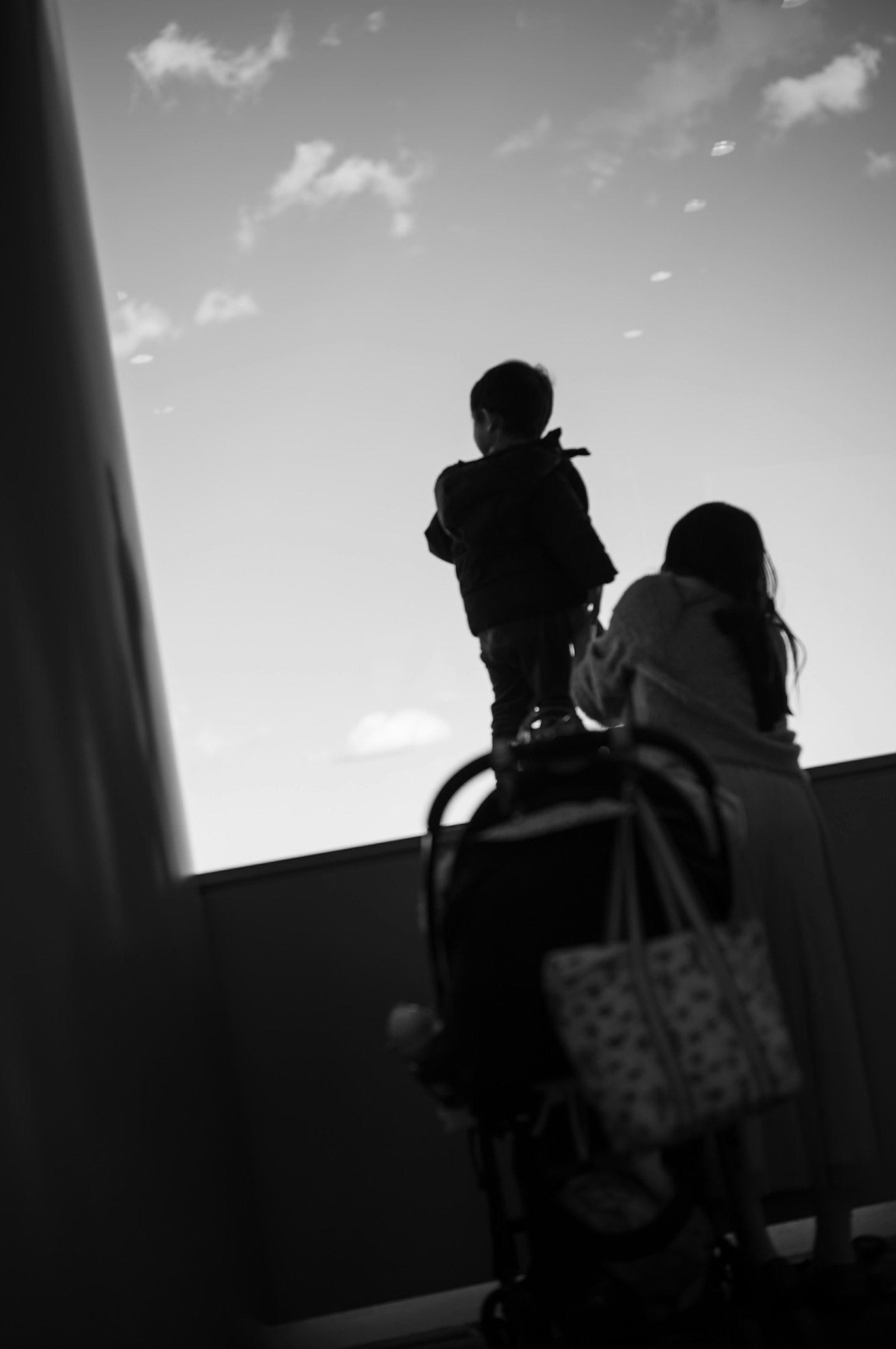 Silhouette eines Kindes, das zum Himmel schaut, mit einem Erwachsenen dahinter, der einen Kinderwagen hält