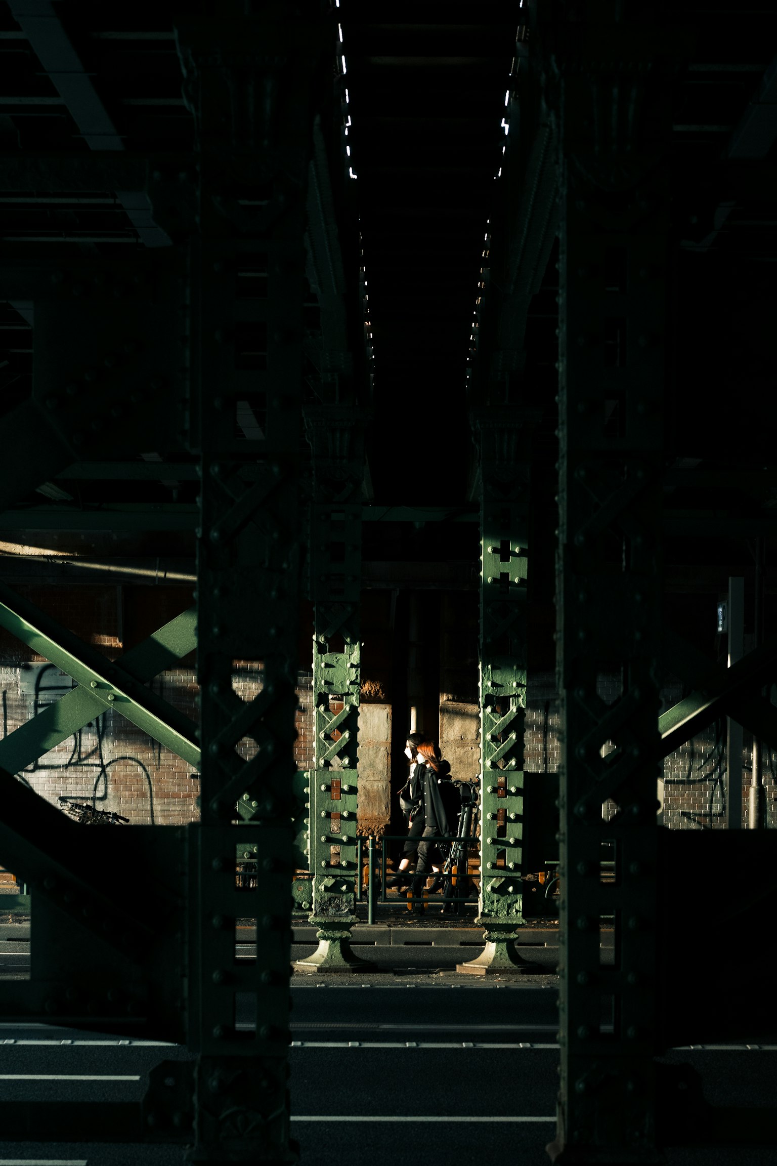 A person standing in a dark environment under a railway bridge with green support pillars
