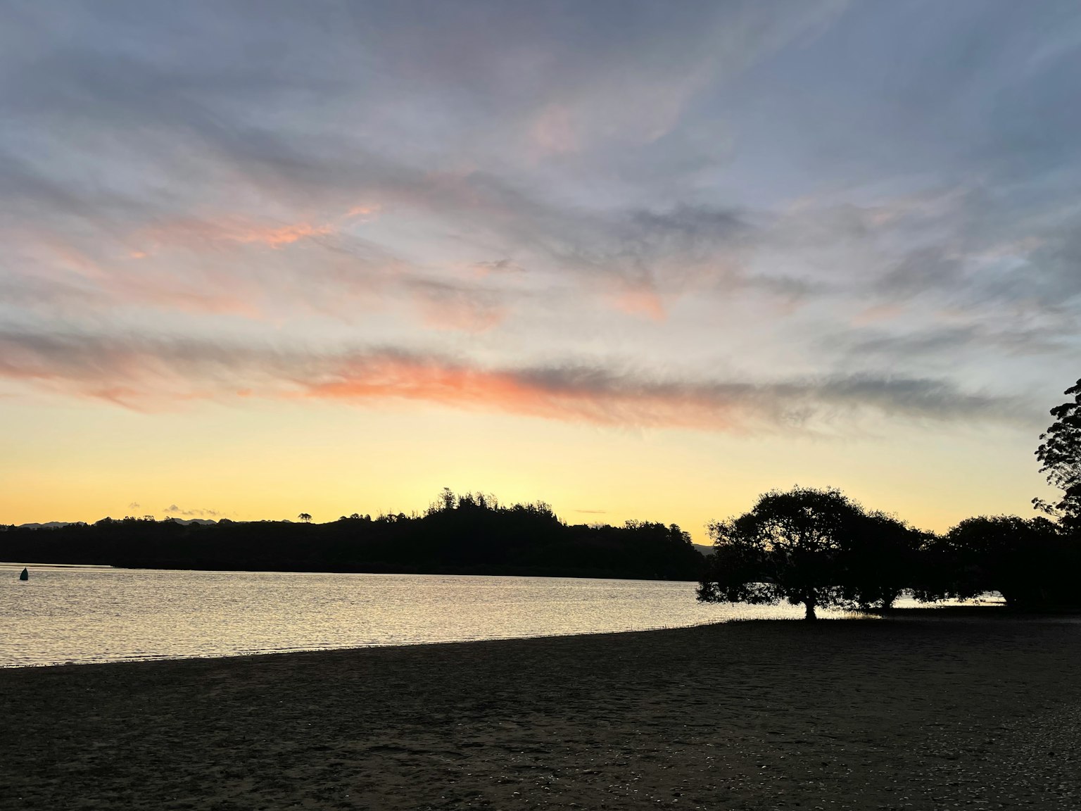 Vista serena al lago con un tramonto che si riflette sull'acqua, colline e alberi in lontananza