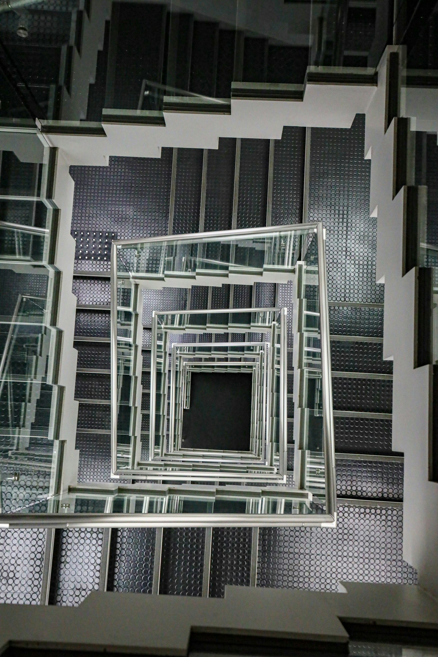 Vue de haut d'un escalier en spirale avec des rampes en verre transparent et des marches noires