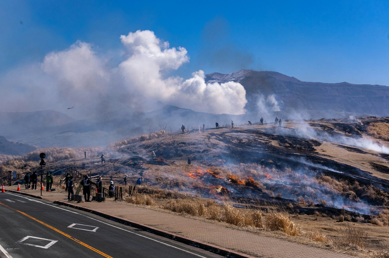 Landschaft eines Waldbrandes mit aufsteigendem Rauch und versammelten Menschen