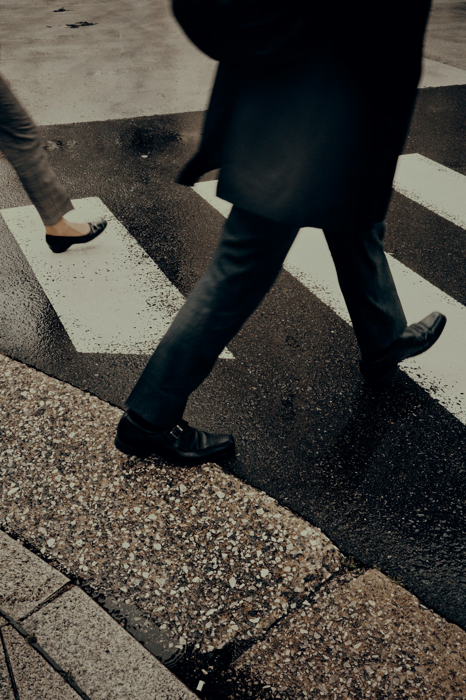 Close-up of two pairs of feet walking on a crosswalk with simple striped lines