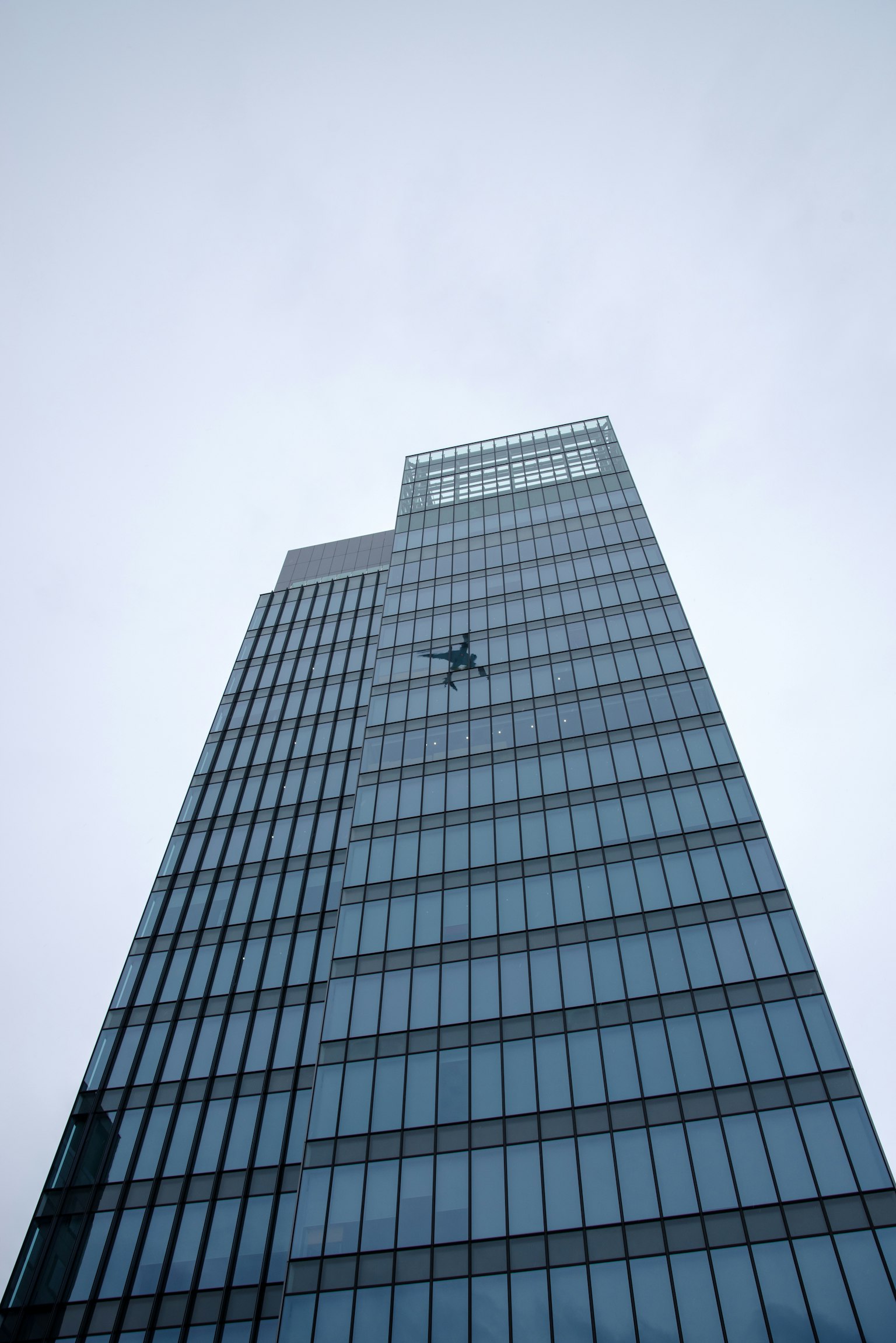 在阴云密布的天空下攀爬摩天大楼玻璃外墙的人