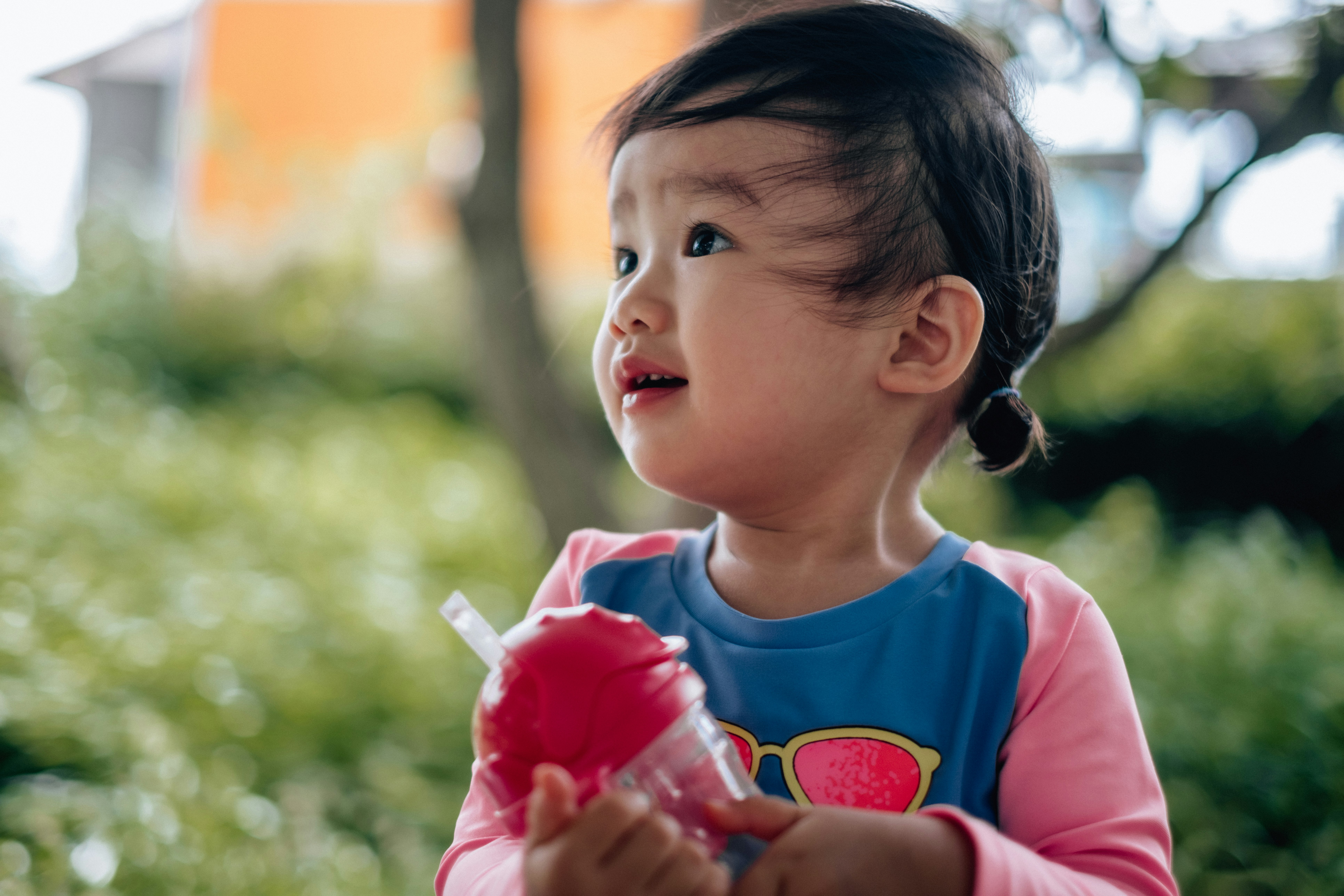 Side profile of a young child holding a drink in a park