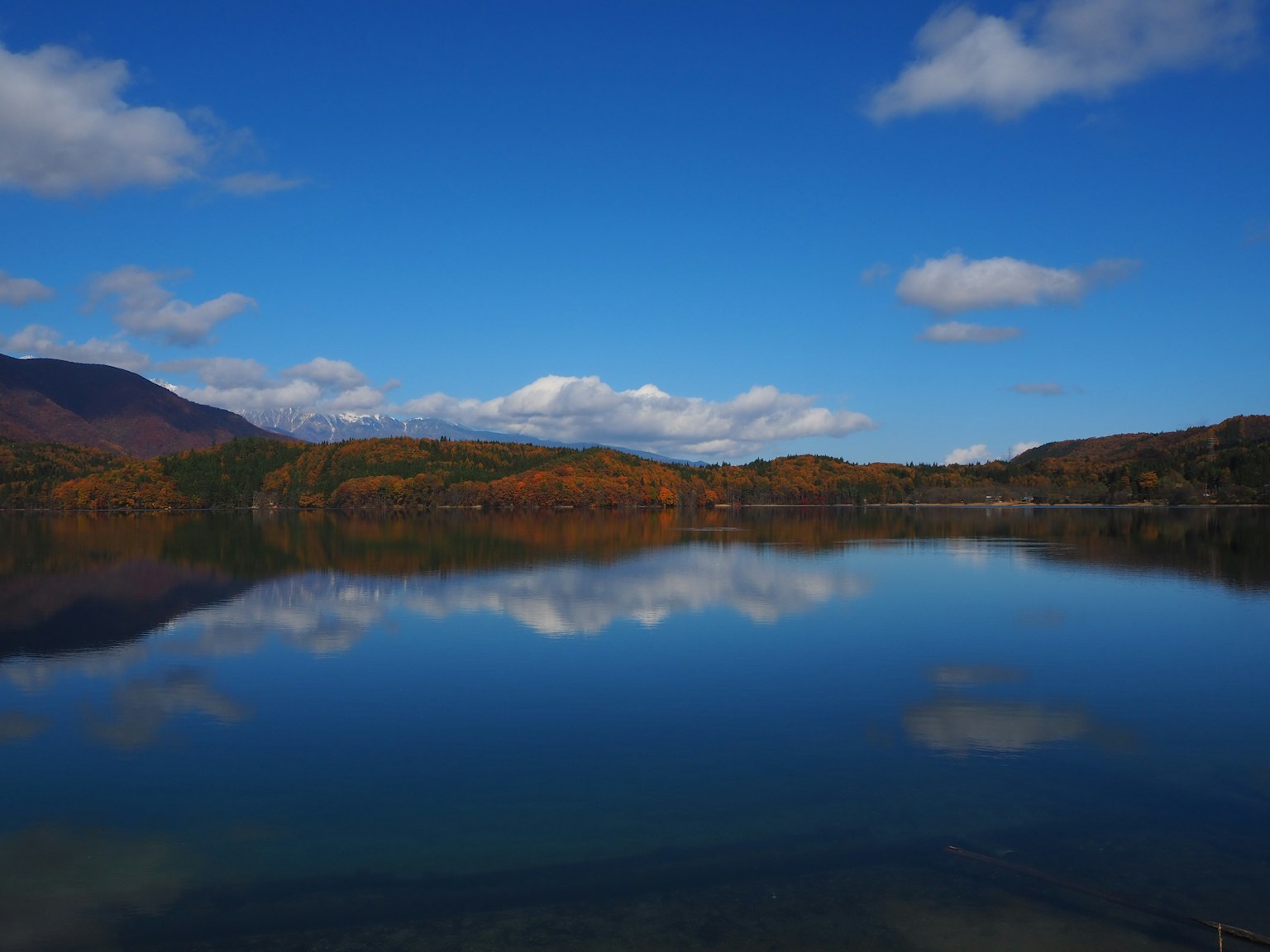 Pemandangan tenang danau yang mencerminkan langit biru dan awan warna musim gugur pegunungan