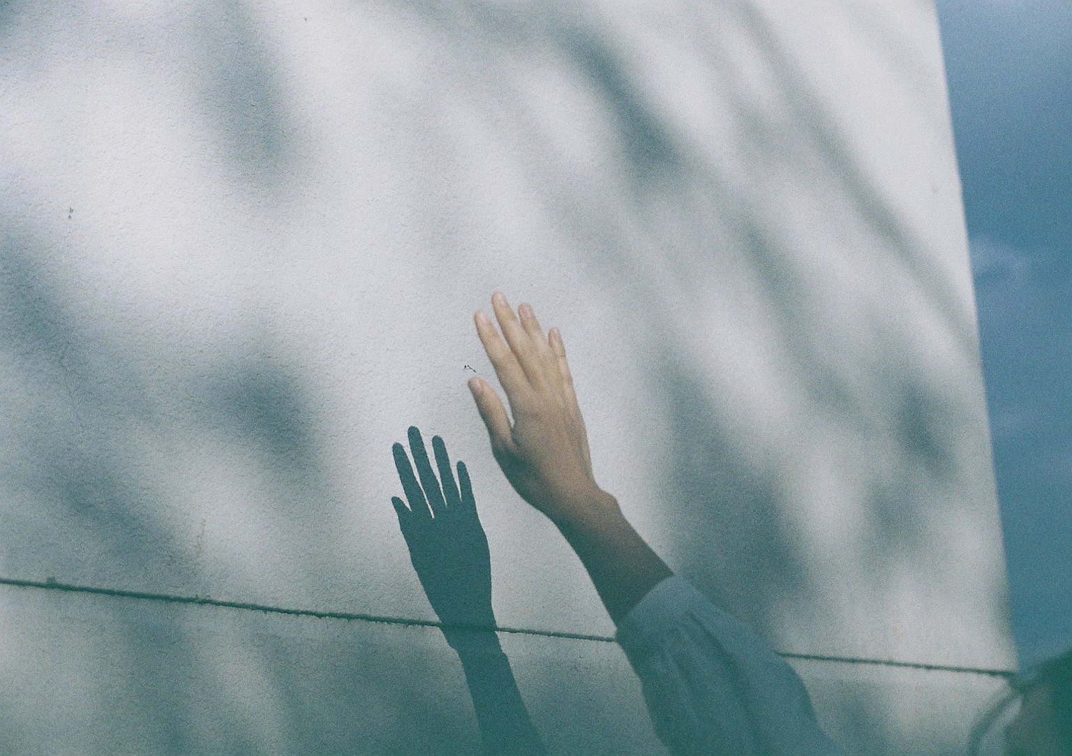 Una mano che si estende verso un muro bianco con ombre proiettate