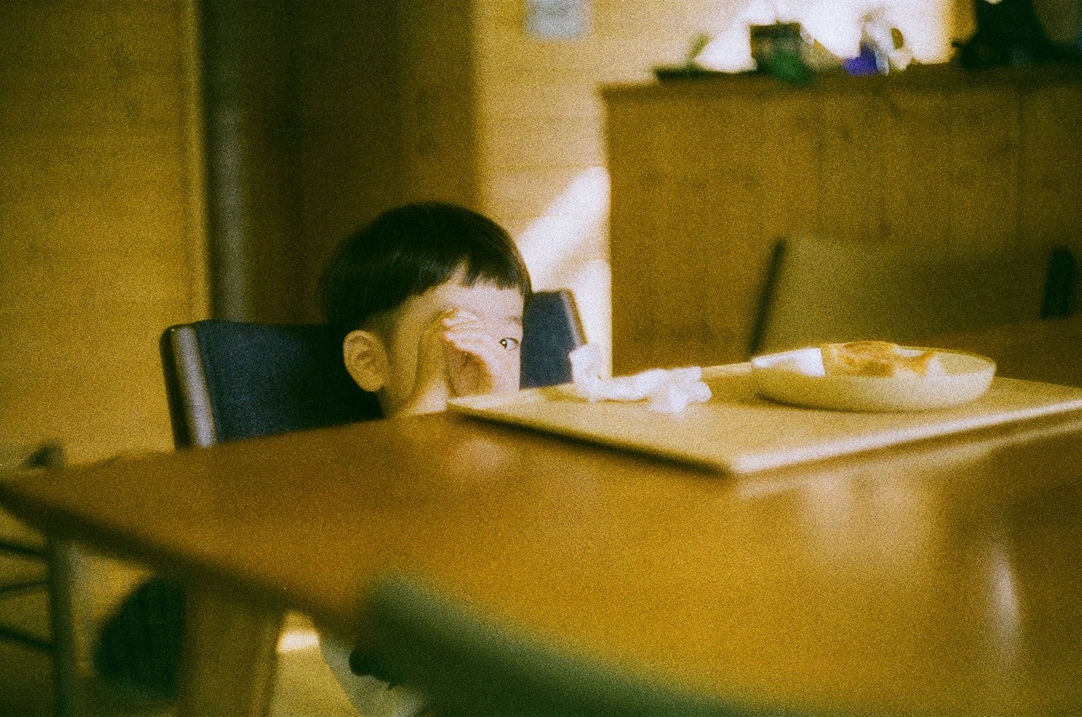 テーブルの前に座っている子供が食べ物を見つめているシーン