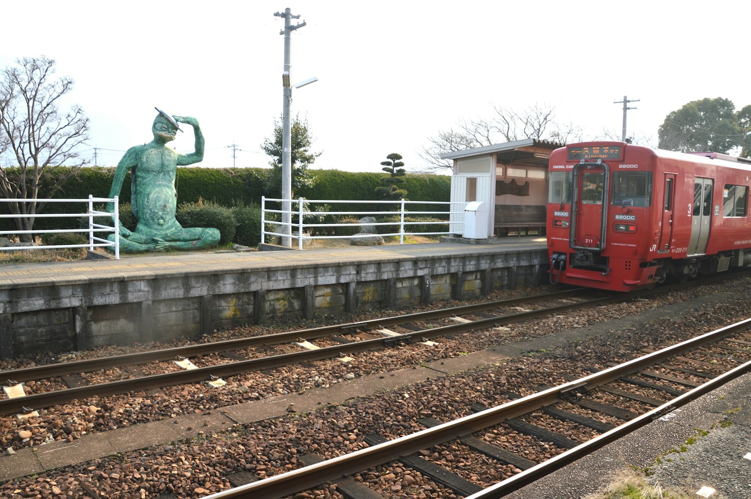 Vista panoramica di un treno rosso in una stazione con una statua in bronzo