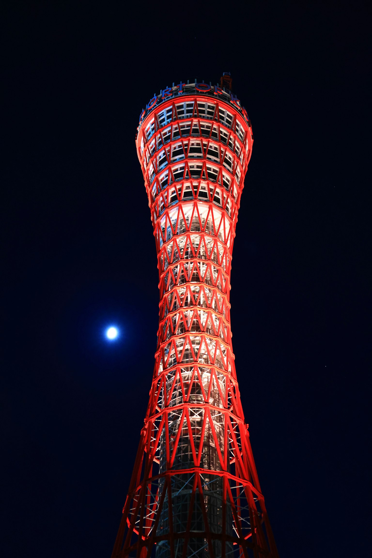 Kobe-Turm bei Nacht in Rot beleuchtet mit sichtbarem Mond