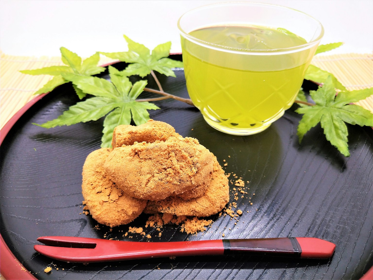 Green tea and Japanese sweets arranged on a black plate with green leaves