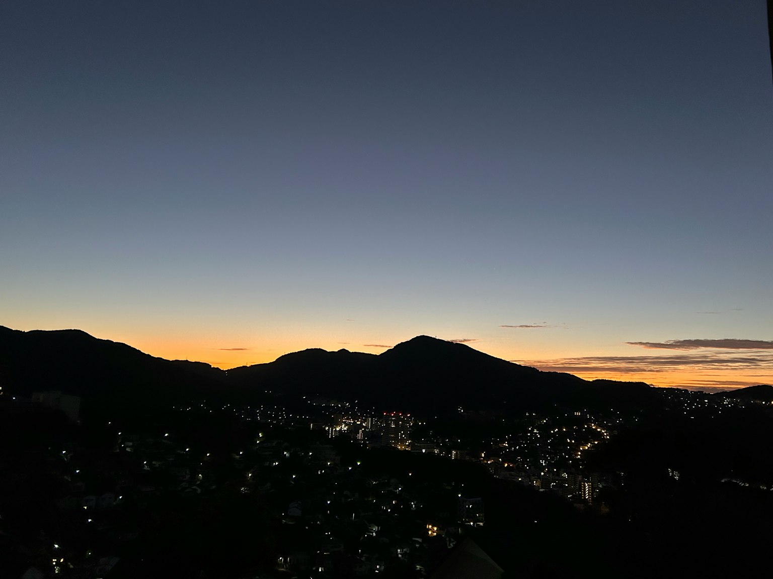 Silhouette of mountains against a twilight sky with city lights