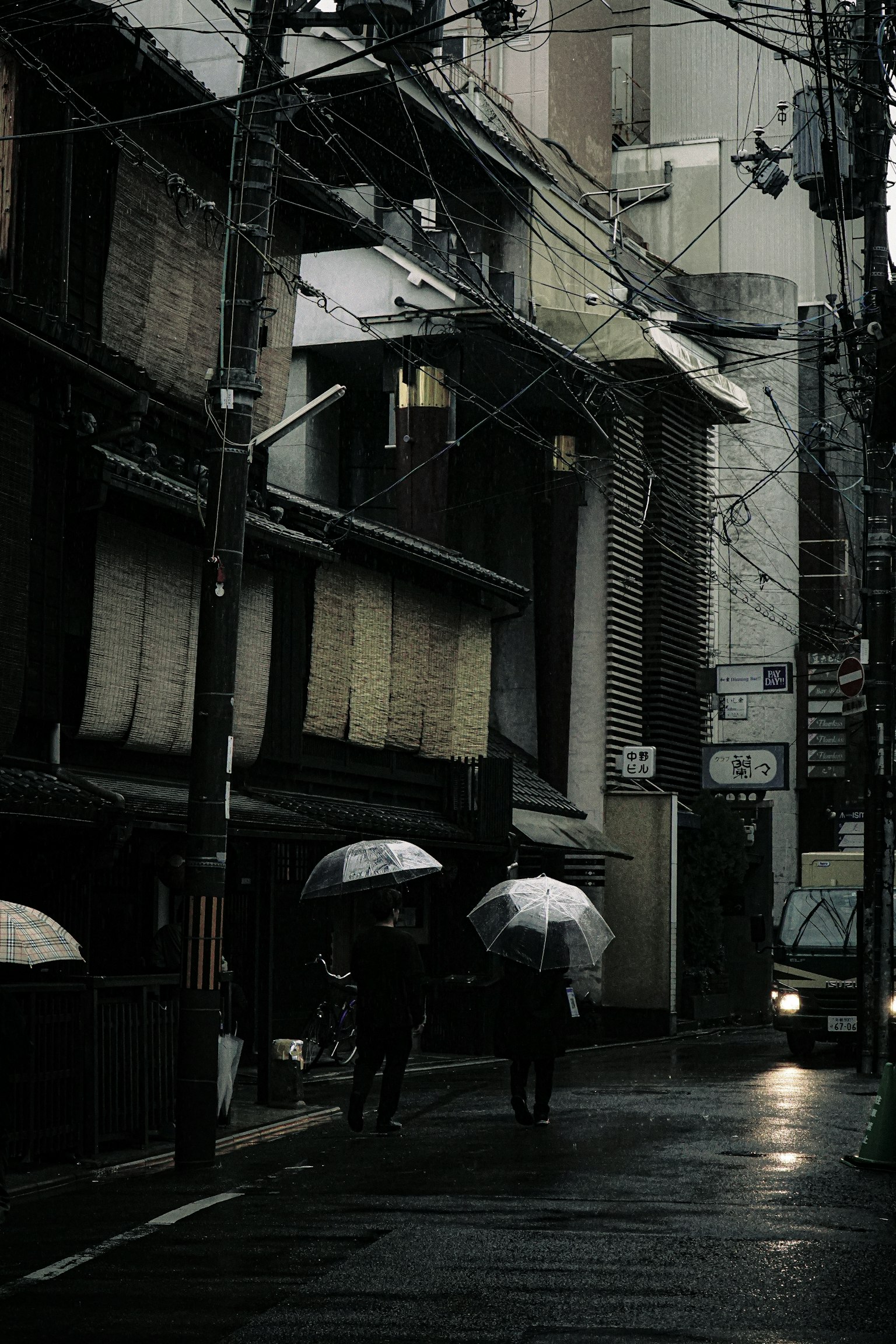 Scene of people walking with umbrellas in the rain narrow street lined with traditional buildings