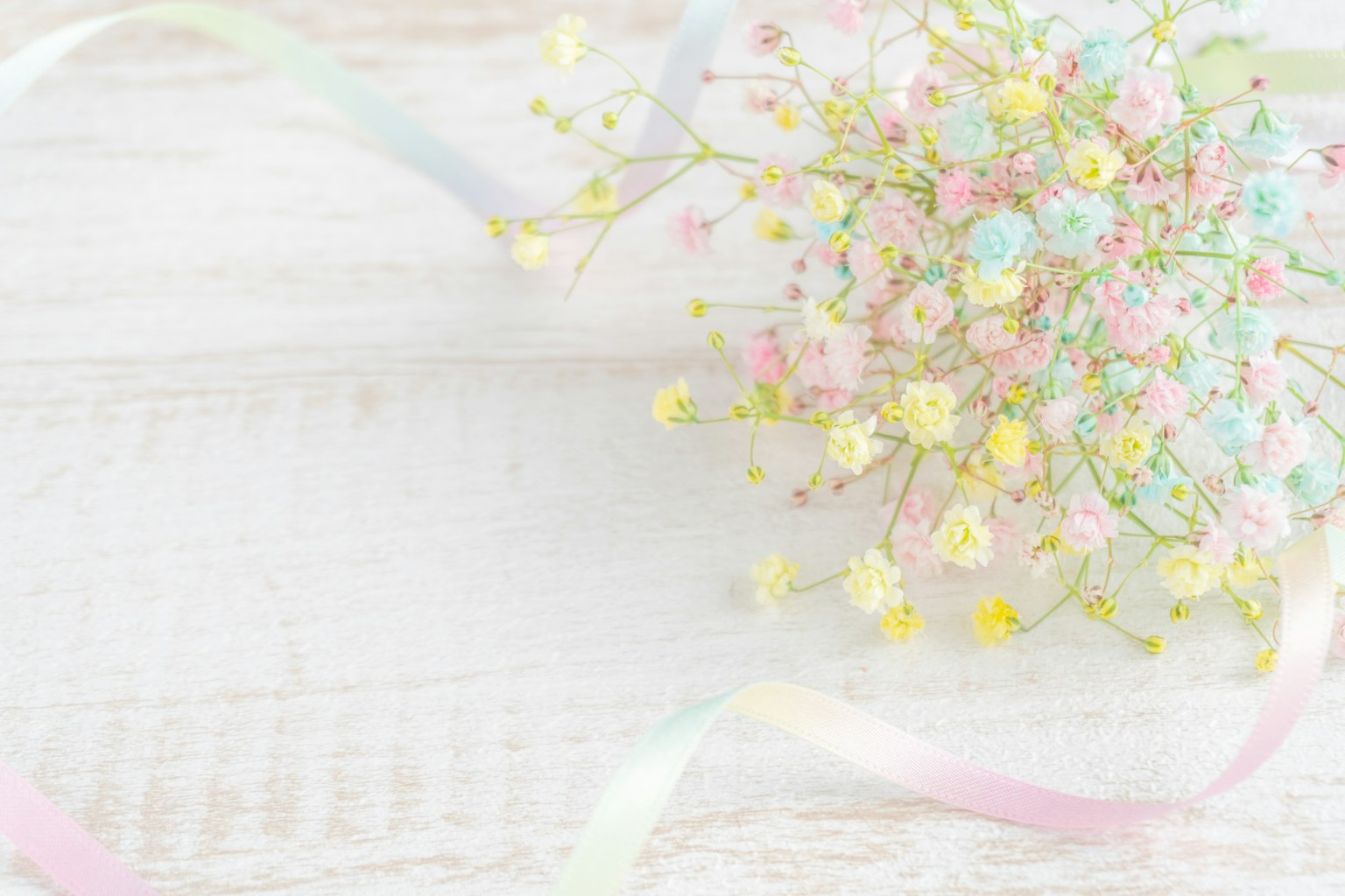 Delicate arrangement of pastel flowers with ribbons on a light wooden background
