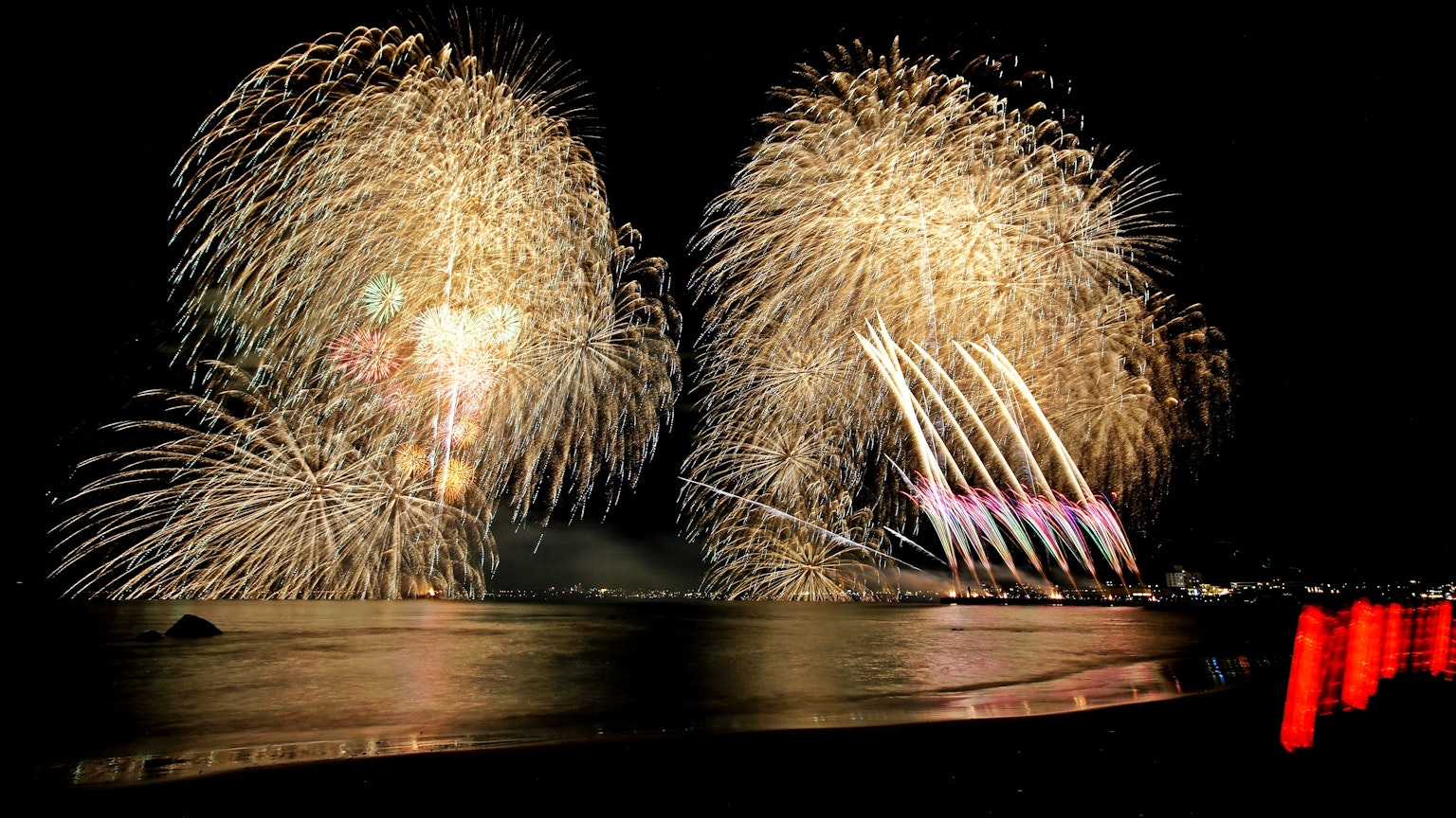 Spettacolo di fuochi d'artificio colorati sopra l'oceano di notte con riflessi sull'acqua