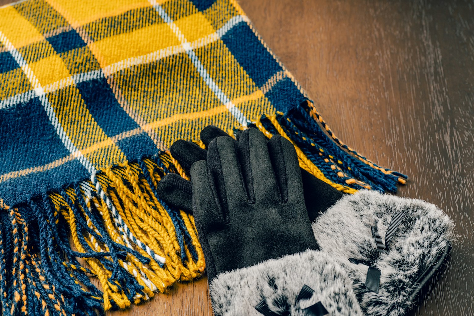 Ein gelb-blau karierter Schal mit schwarzen Handschuhen auf einem Holztisch