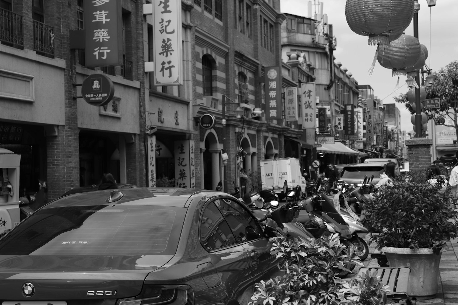 黑白街景，有停放的汽车和摩托车