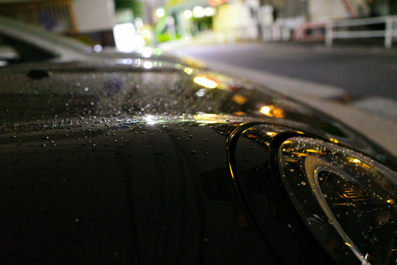 夜の街並みを背景にした濡れた車のボディのクローズアップ