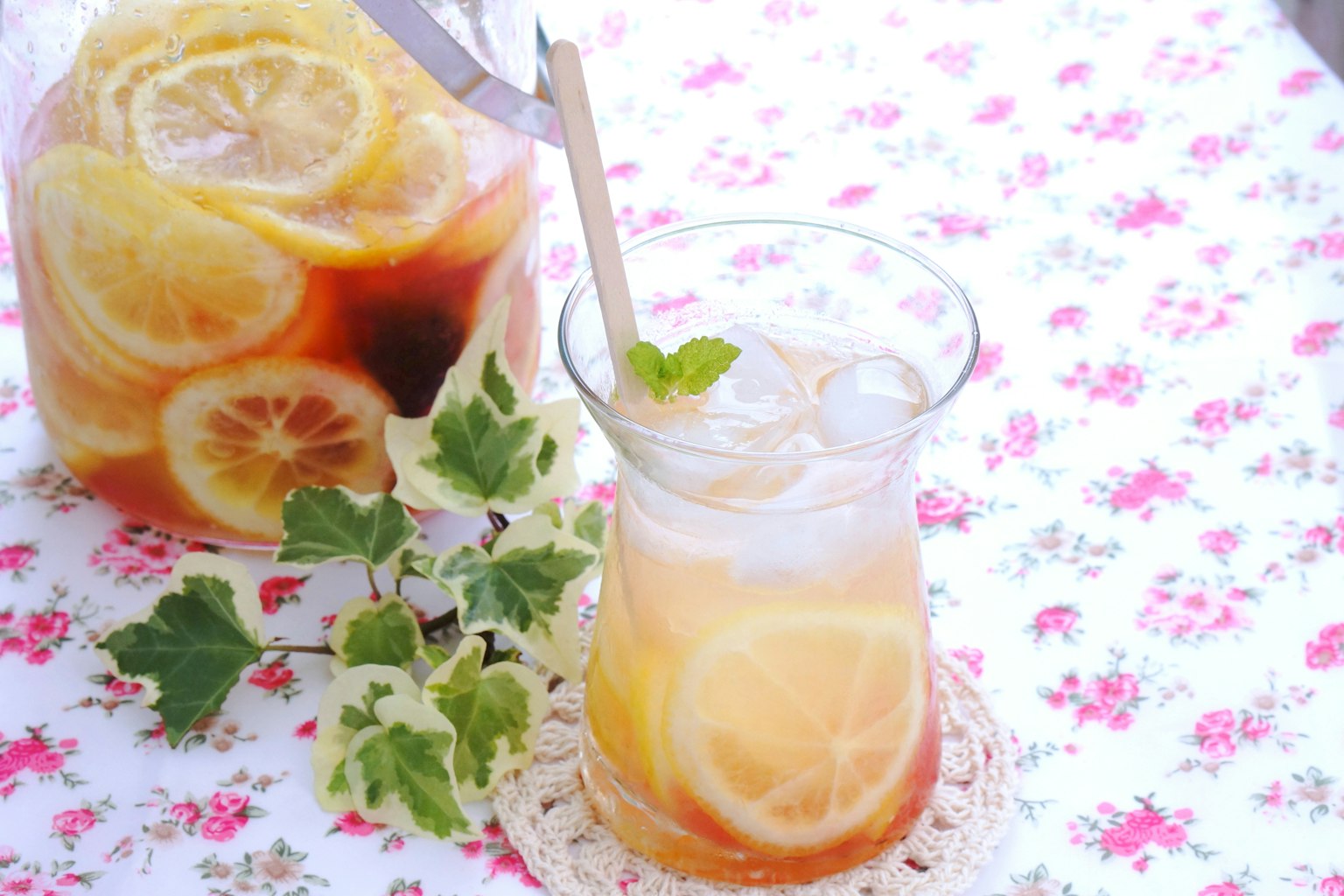 Glass of iced tea with lemon and mint beside a pitcher