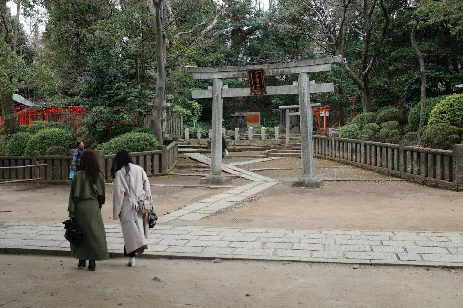 Deux femmes marchant dans un parc verdoyant avec une porte torii