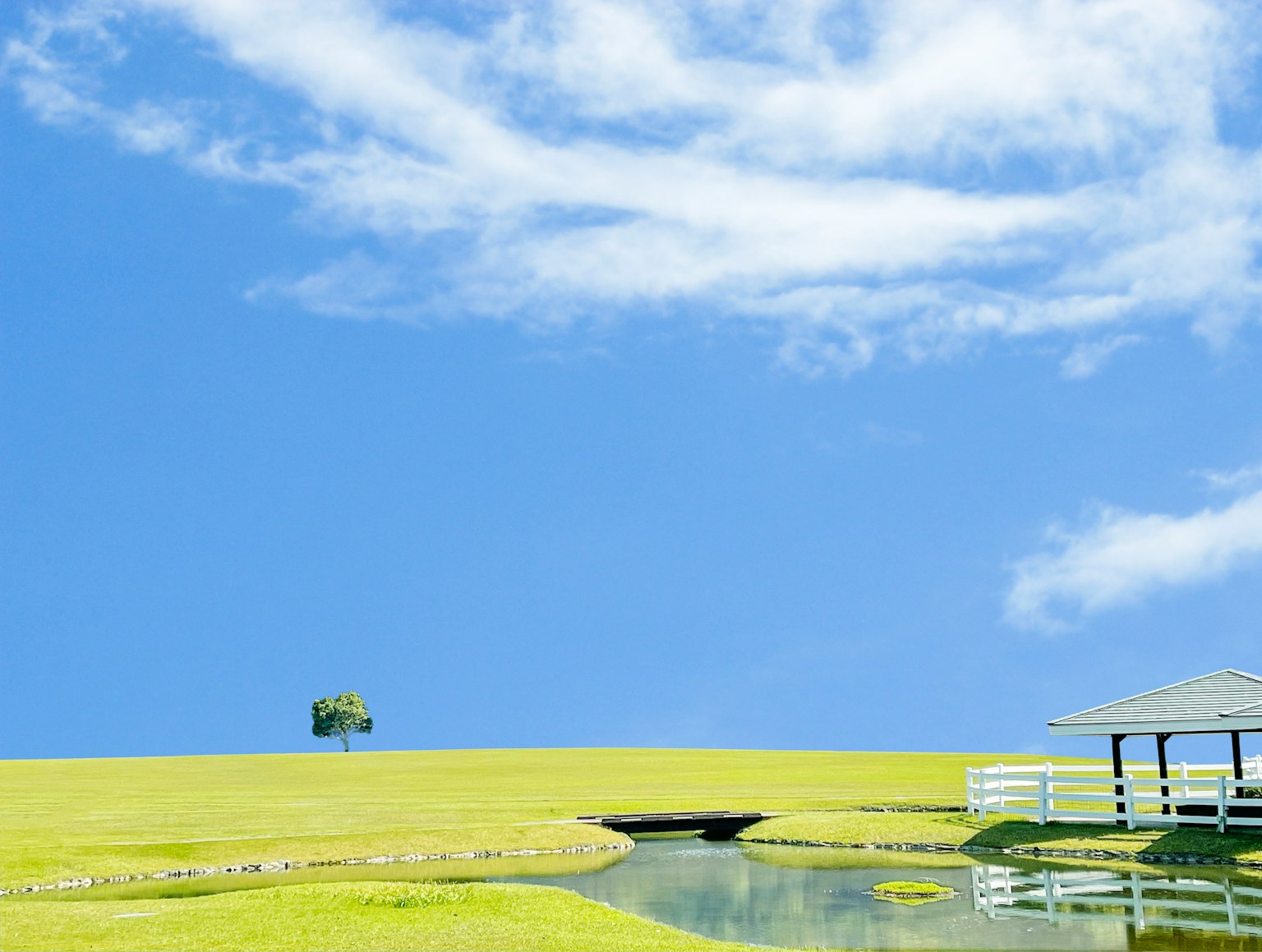 Paisaje con colinas verdes y un estanque bajo un cielo azul