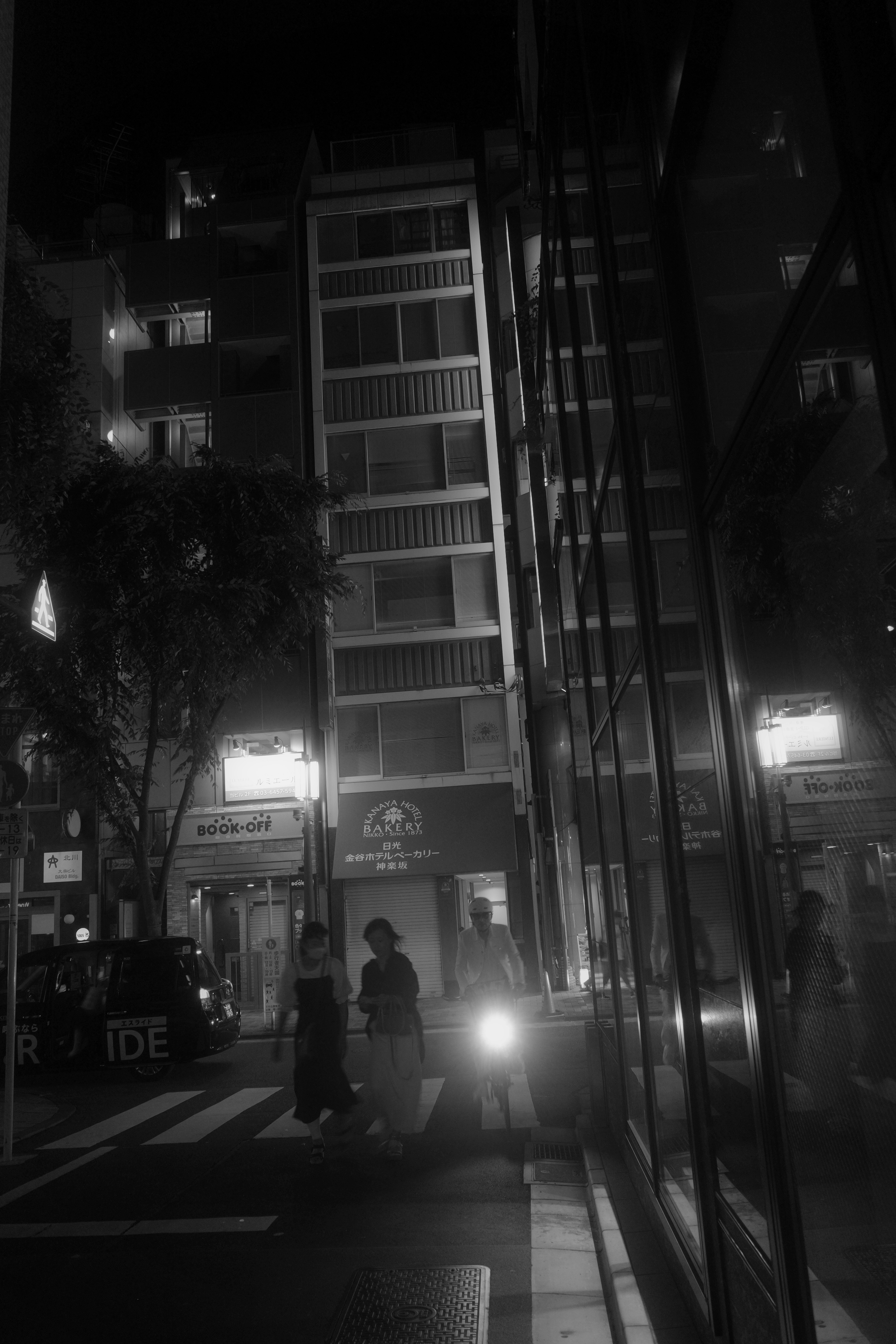 persimpangan malam hari dengan pejalan kaki dan gedung-gedung tinggi di sepanjang jalan sempit