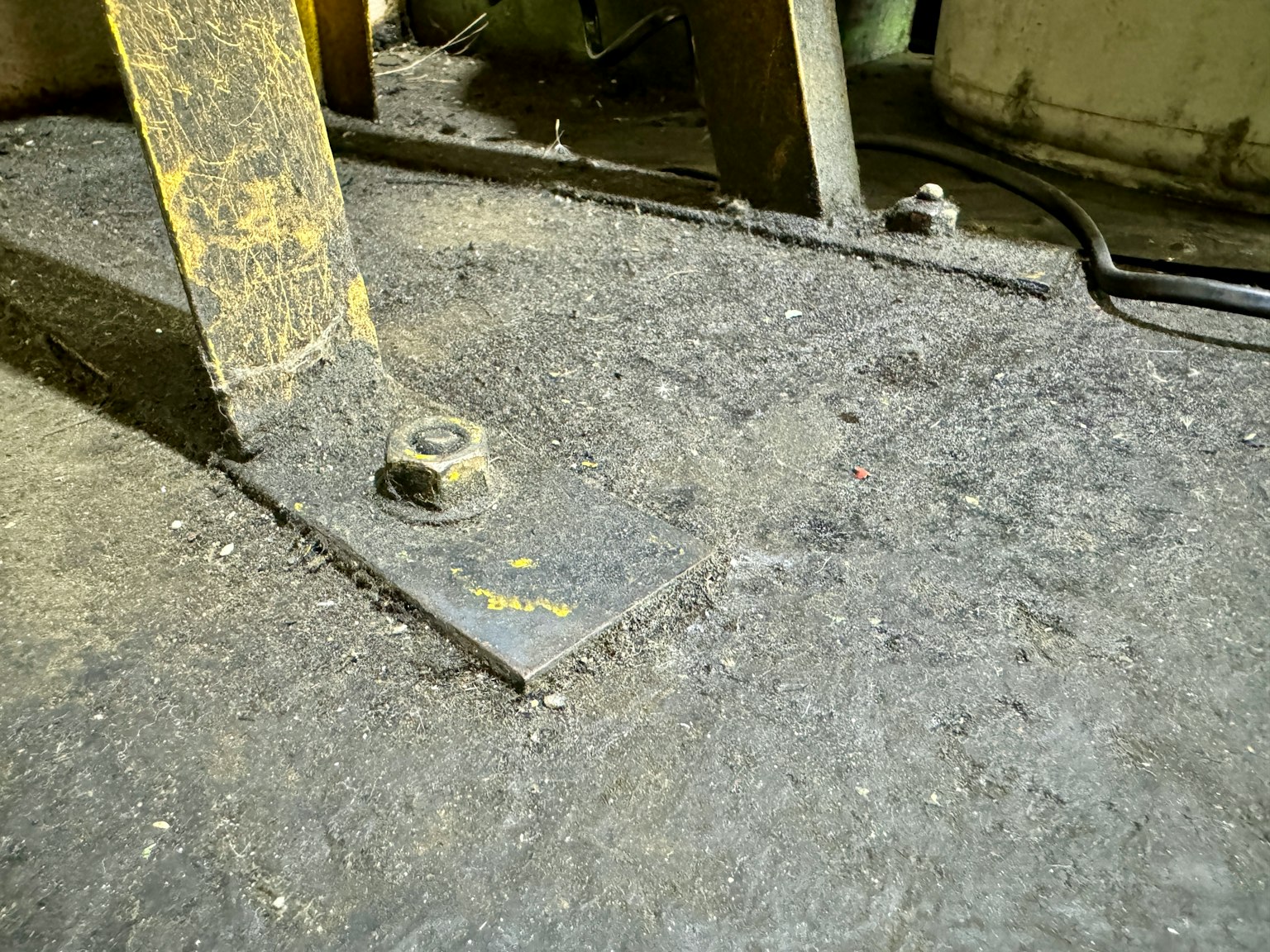 Nahaufnahme einer Metallplatte und einer Schraube auf einem staubigen Fabrikboden