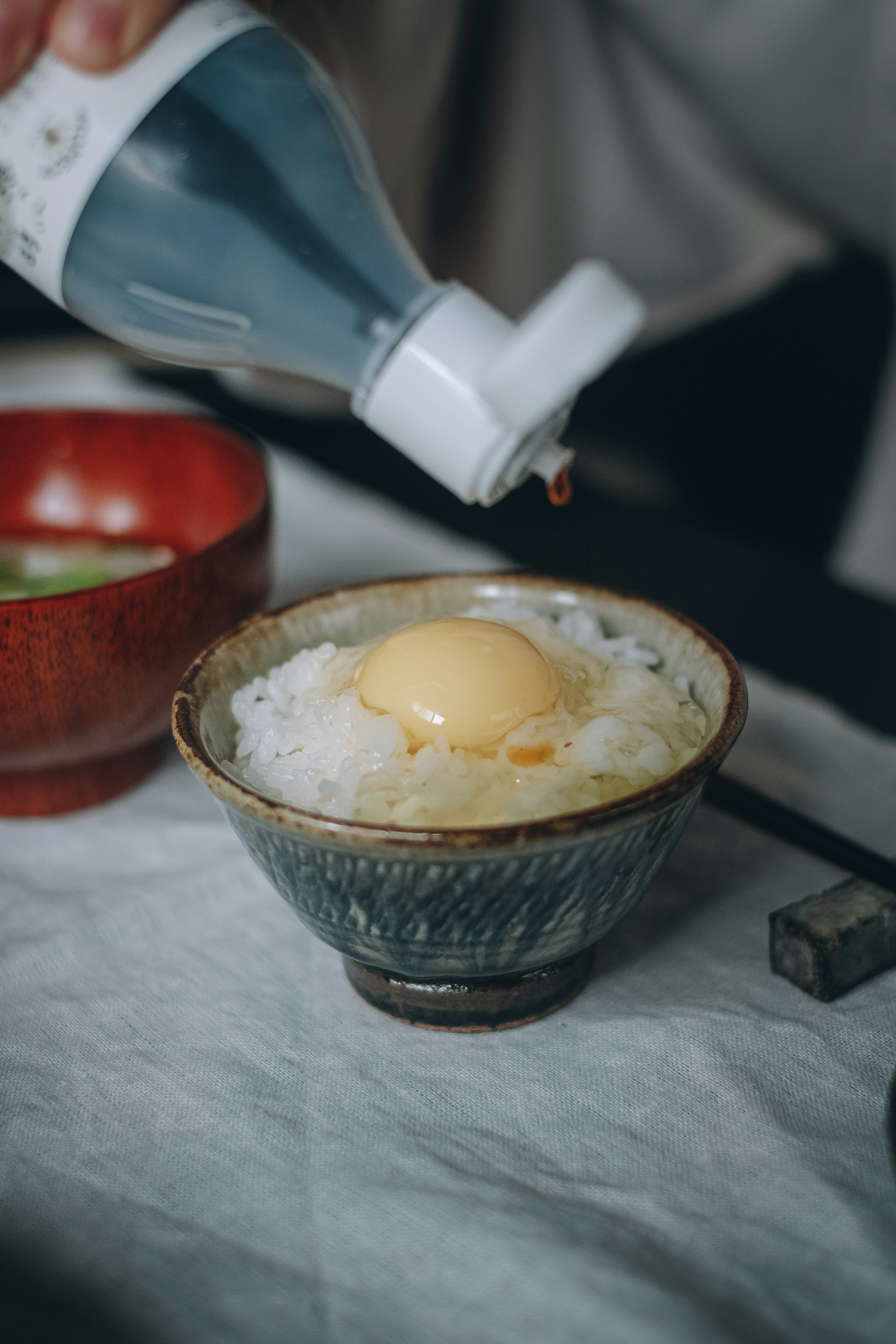 湯気の立つ卵かけご飯に醤油を注ぐ手元