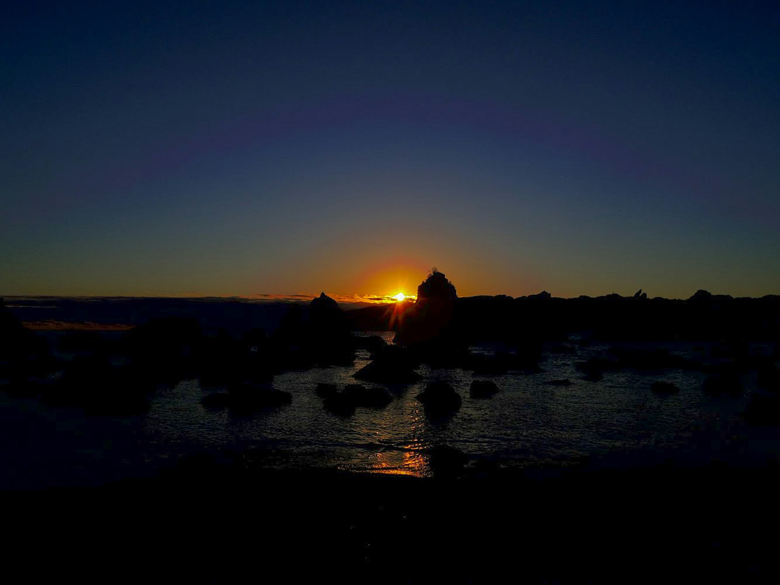 Küstenlandschaft mit Sonnenuntergang zwischen den Felsen sichtbar
