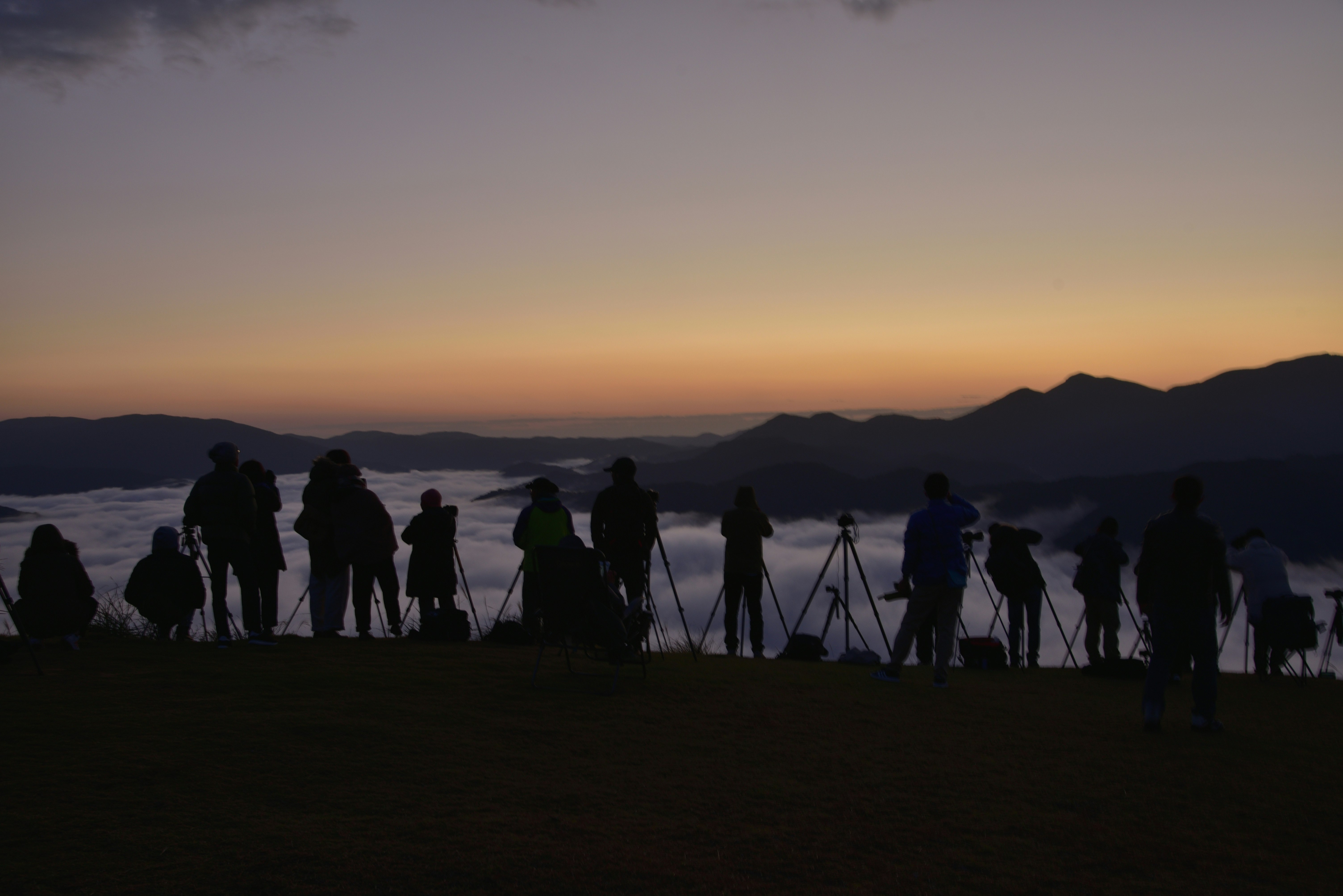 Orang-orang dengan tripod di bukit saat senja, menghadap siluet pegunungan