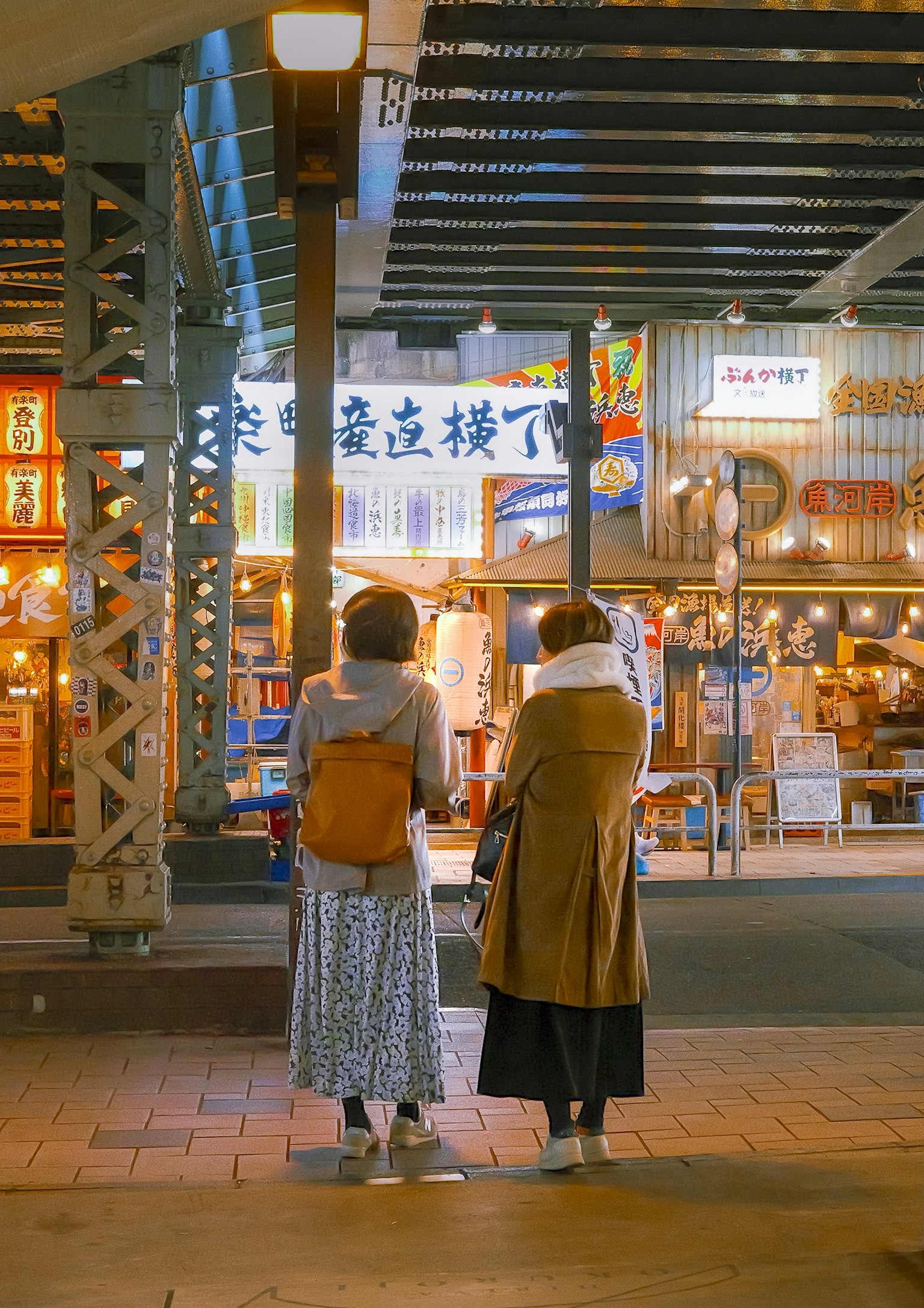 Two women standing in front of shops in a night city scene