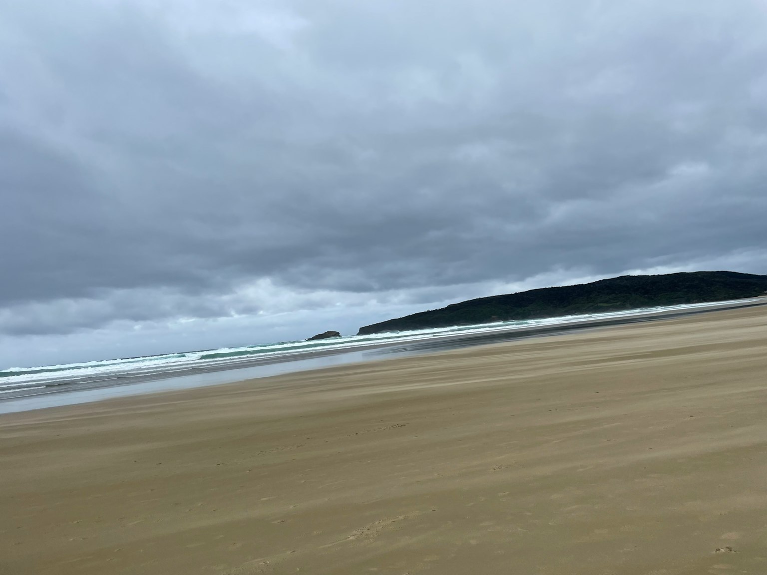 灰色雲層覆蓋的海灘景觀 溫和的波浪輕輕拍打沙灘