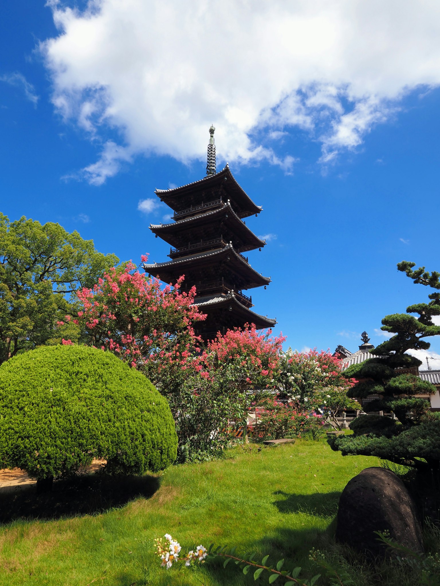 Japanische Pagode umgeben von blühenden Bäumen und lebendigem Grün unter einem blauen Himmel
