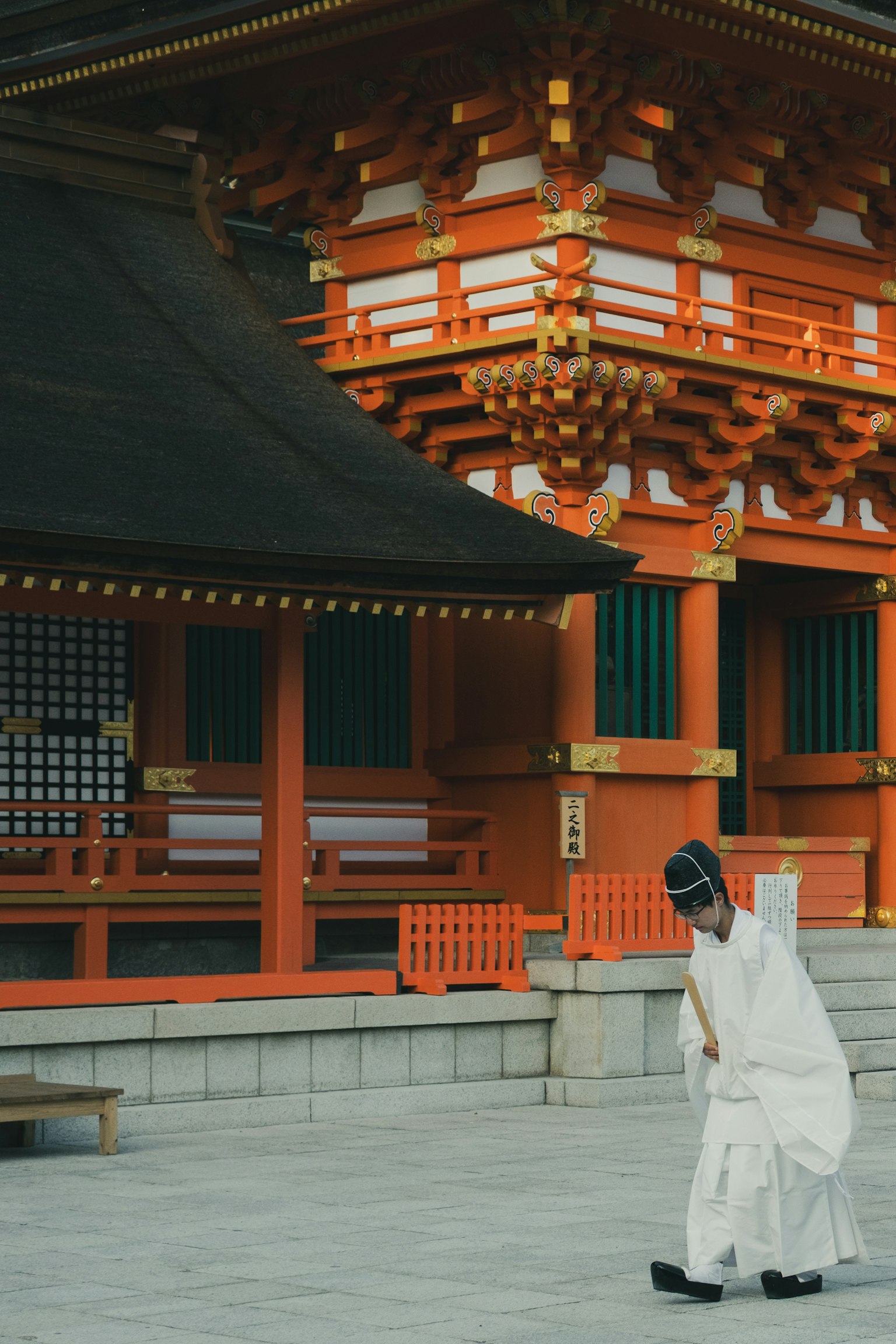 赤い神社の前で白い着物を着た人物が歩いている