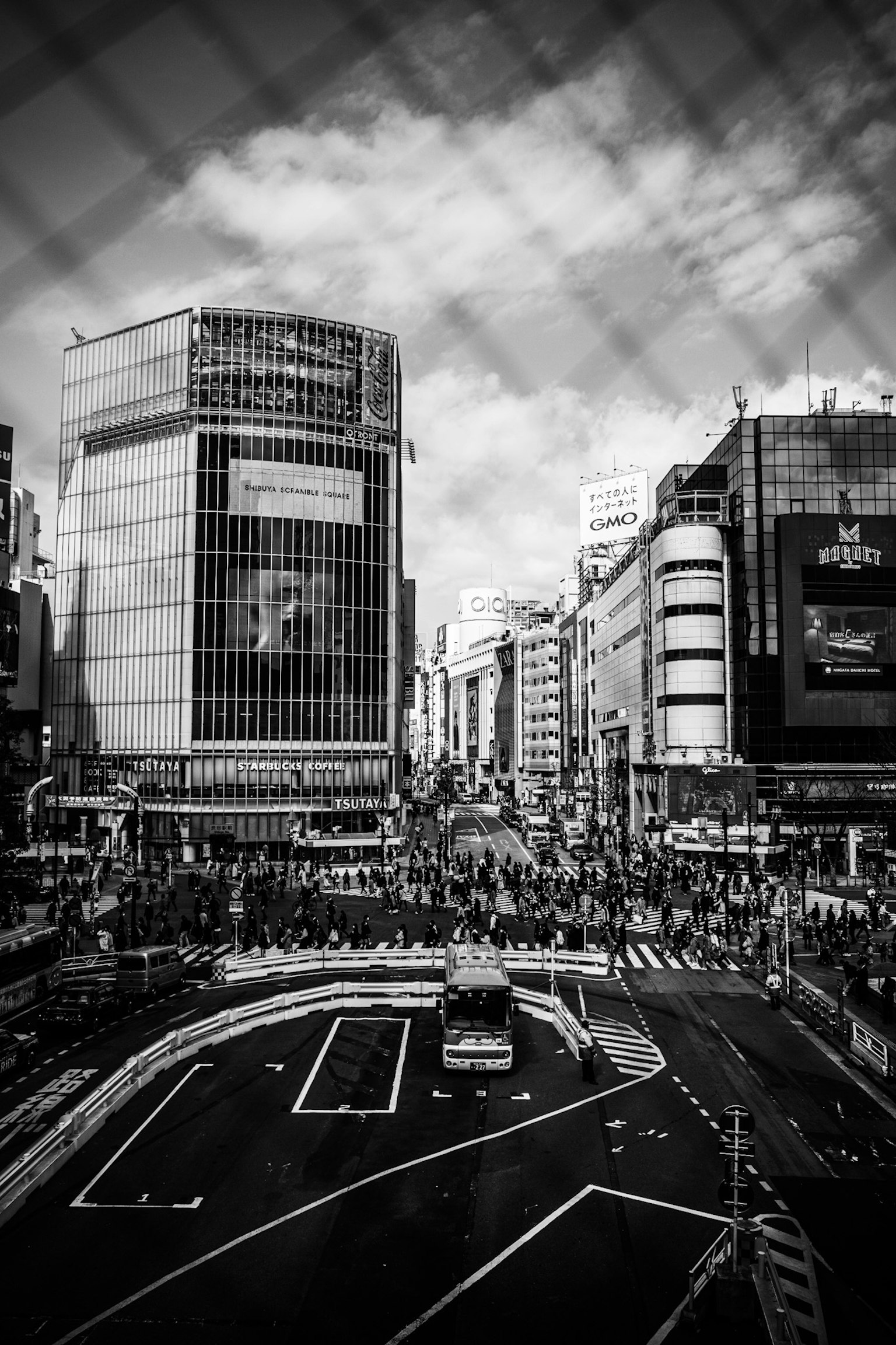 Foto en blanco y negro de Shibuya mostrando una calle concurrida con muchos peatones y vehículos