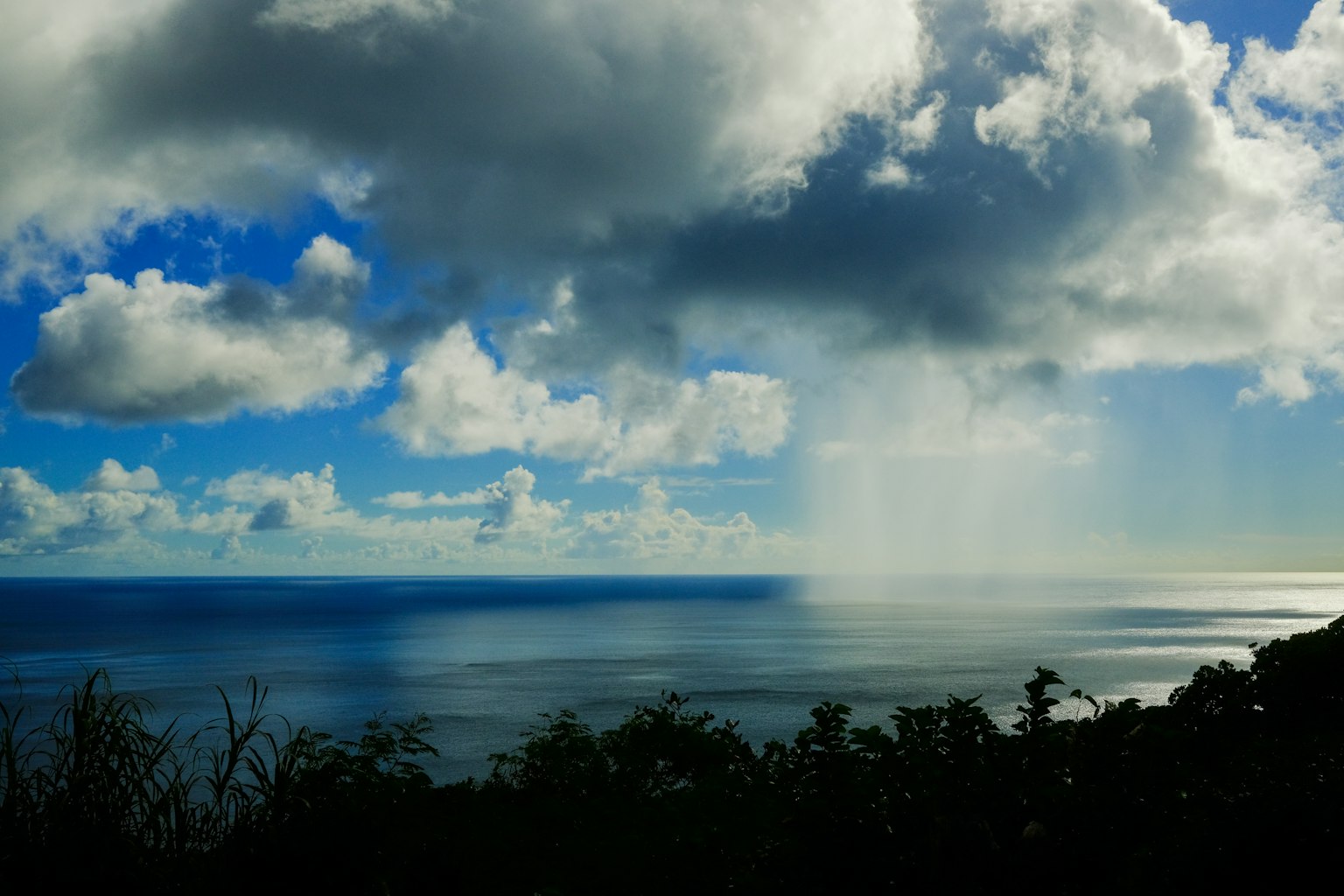 Scenic view of blue ocean and clouds with visible rain falling
