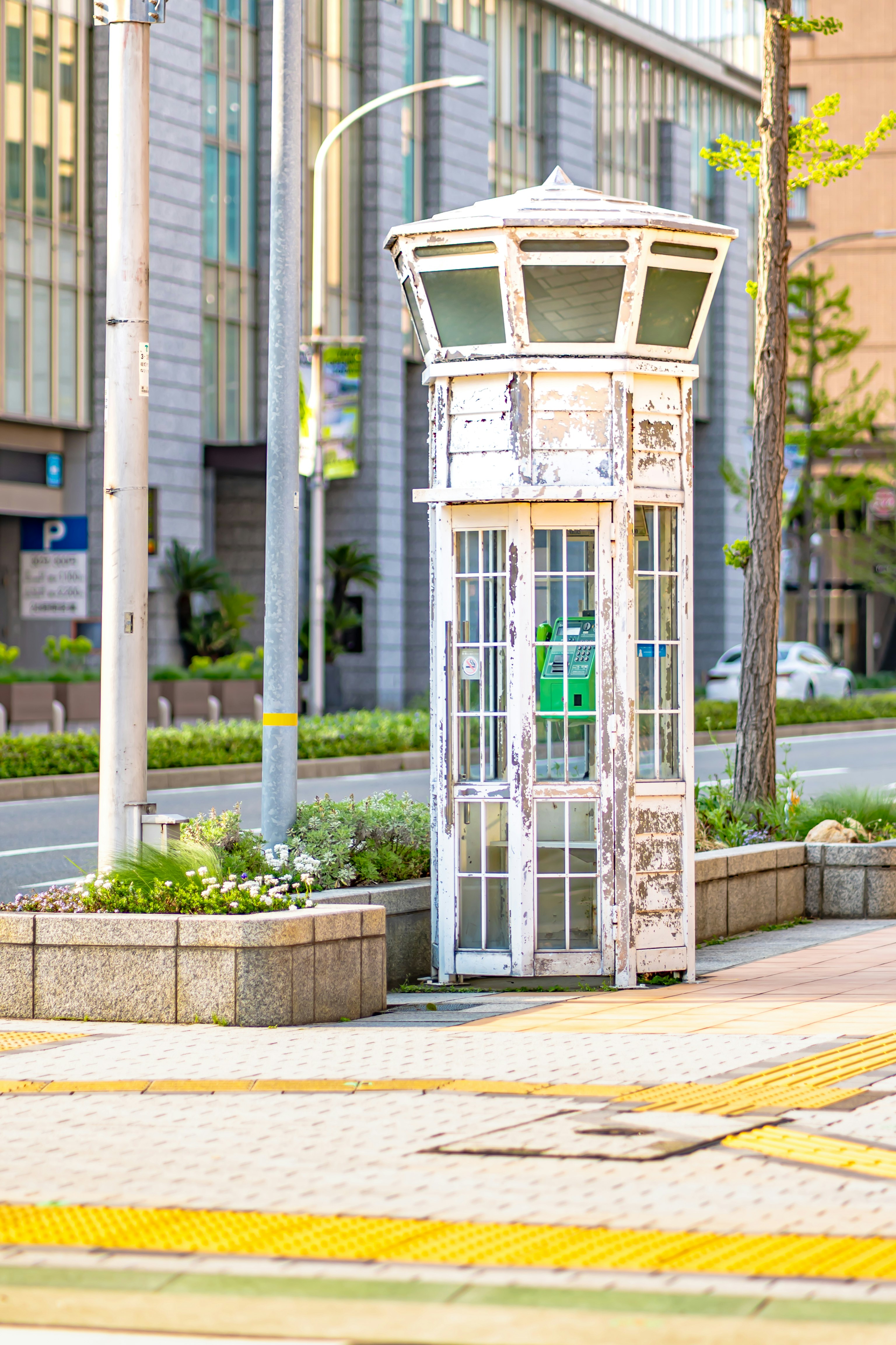 電話ボックスが街の通りに立っている緑の植物が周囲にある