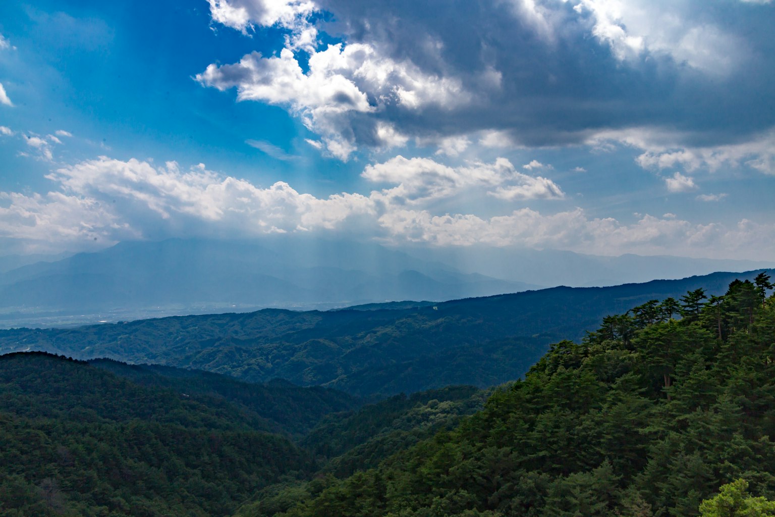 Pemandangan pegunungan dengan langit biru dan awan hutan hijau di lembah