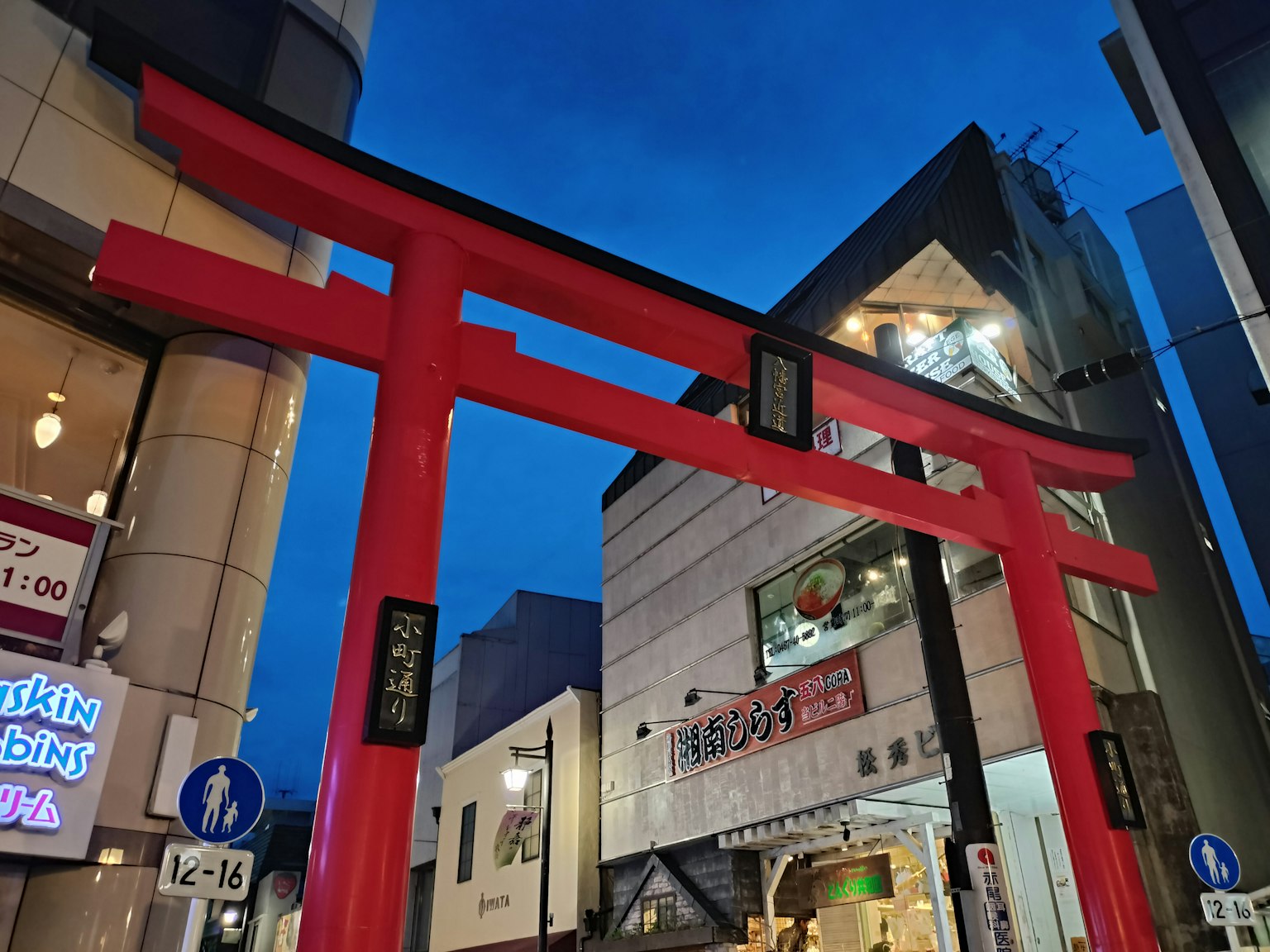Una puerta torii roja se erige en un área comercial bajo el cielo nocturno
