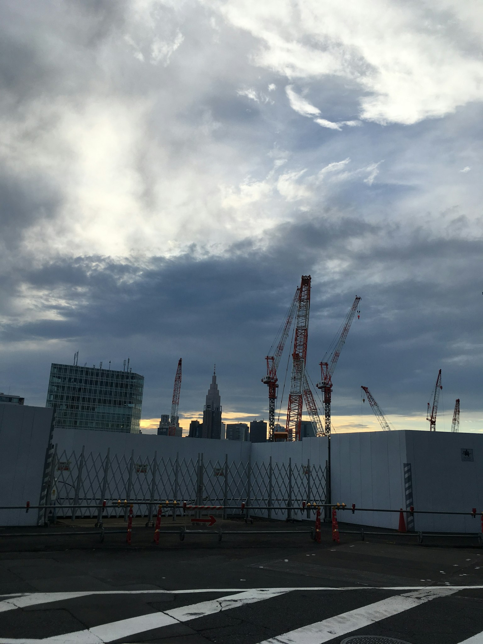 View of a construction site with cranes and skyscrapers under a cloudy sky