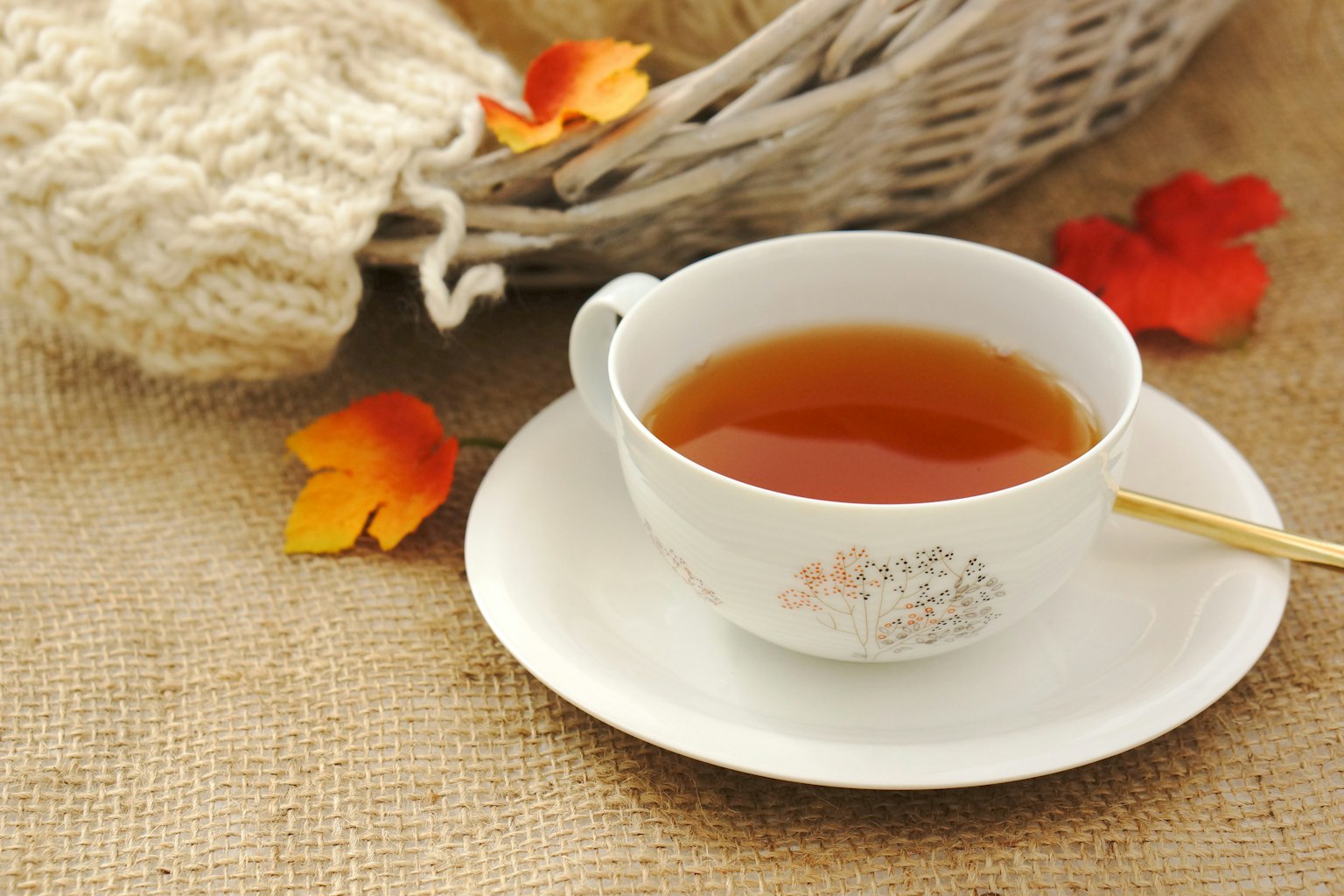 一杯熱茶放在麻布上，旁邊有秋天的葉子和溫暖的毛衣