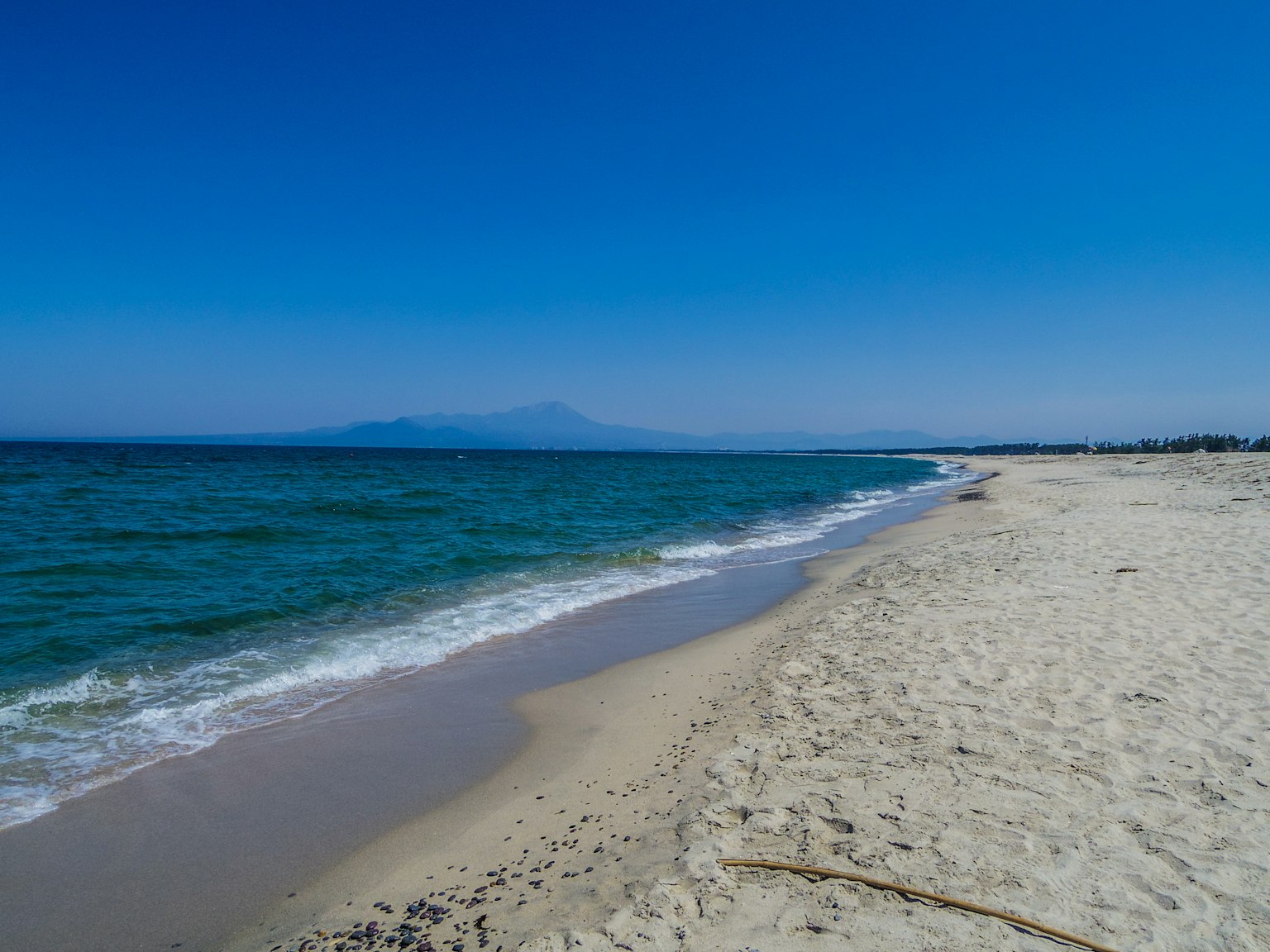 Pemandangan pantai yang indah dengan lautan biru dan pasir putih serta pegunungan di kejauhan