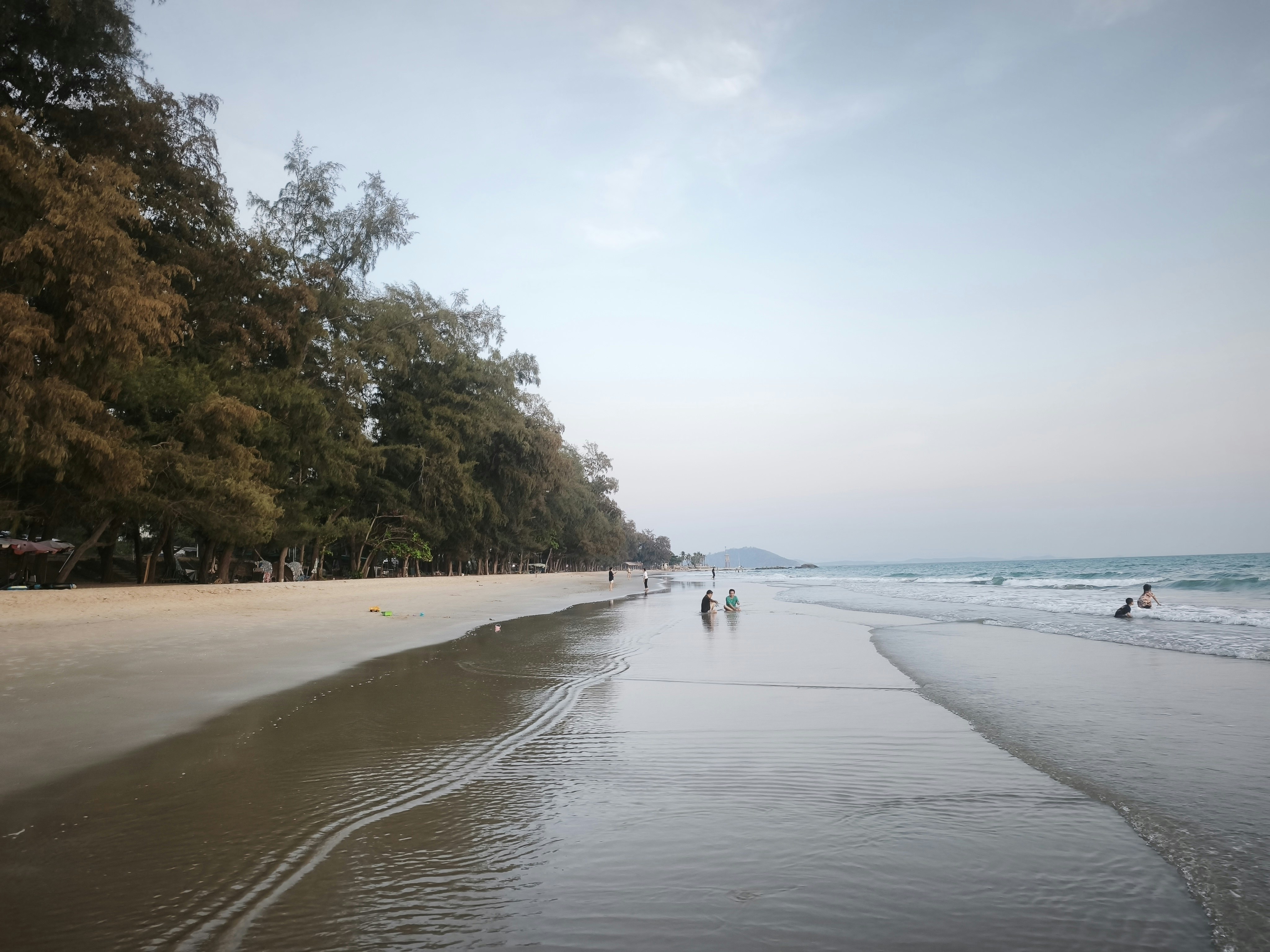 海辺の砂浜を歩く人々と穏やかな波の風景