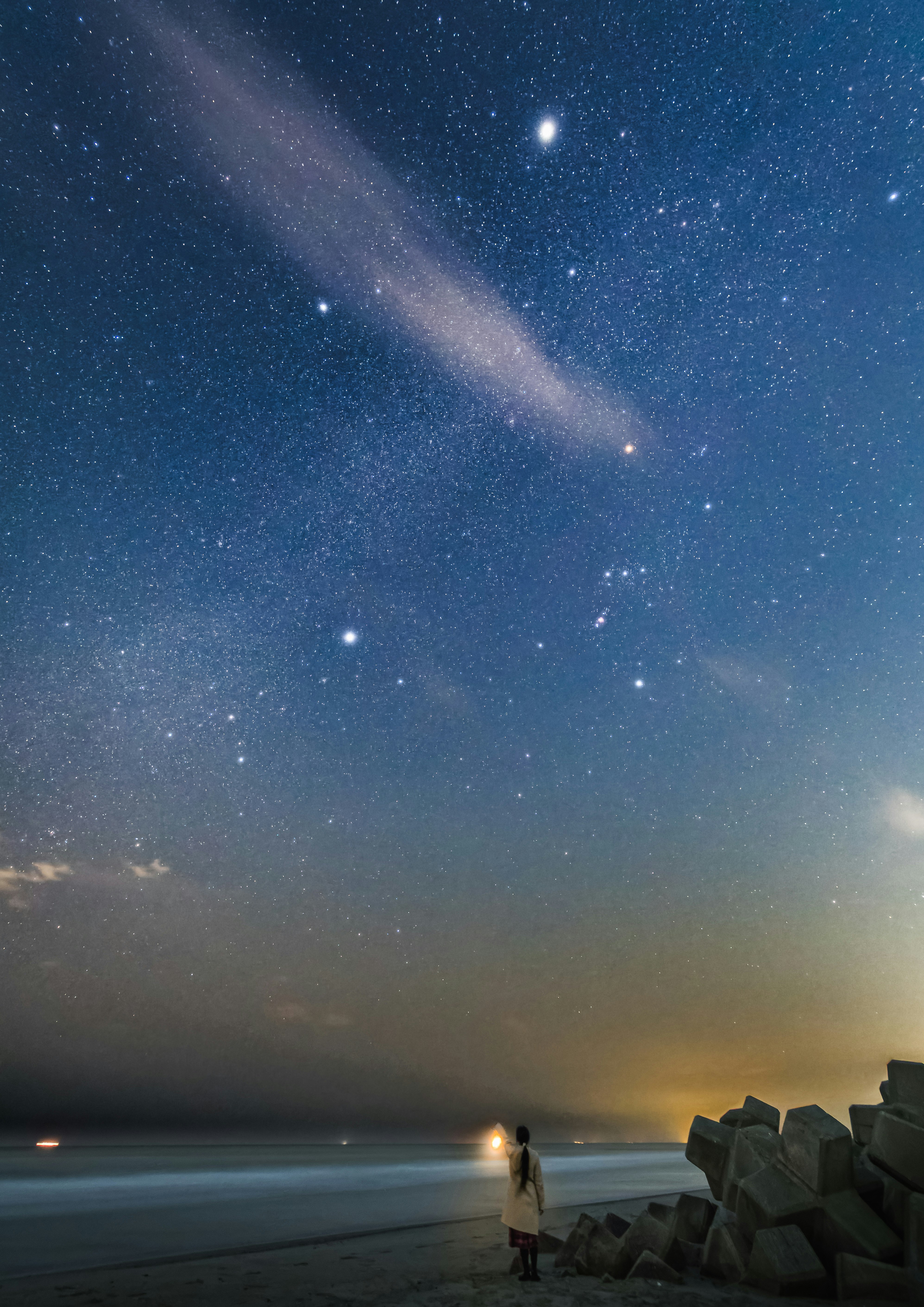 星空の下で立つ人物と海の景色が広がる夜のビーチ