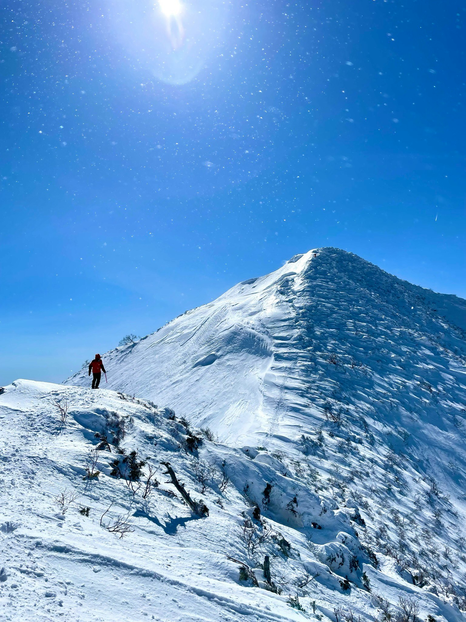 Wanderer auf einem schneebedeckten Berggipfel unter klarem blauen Himmel