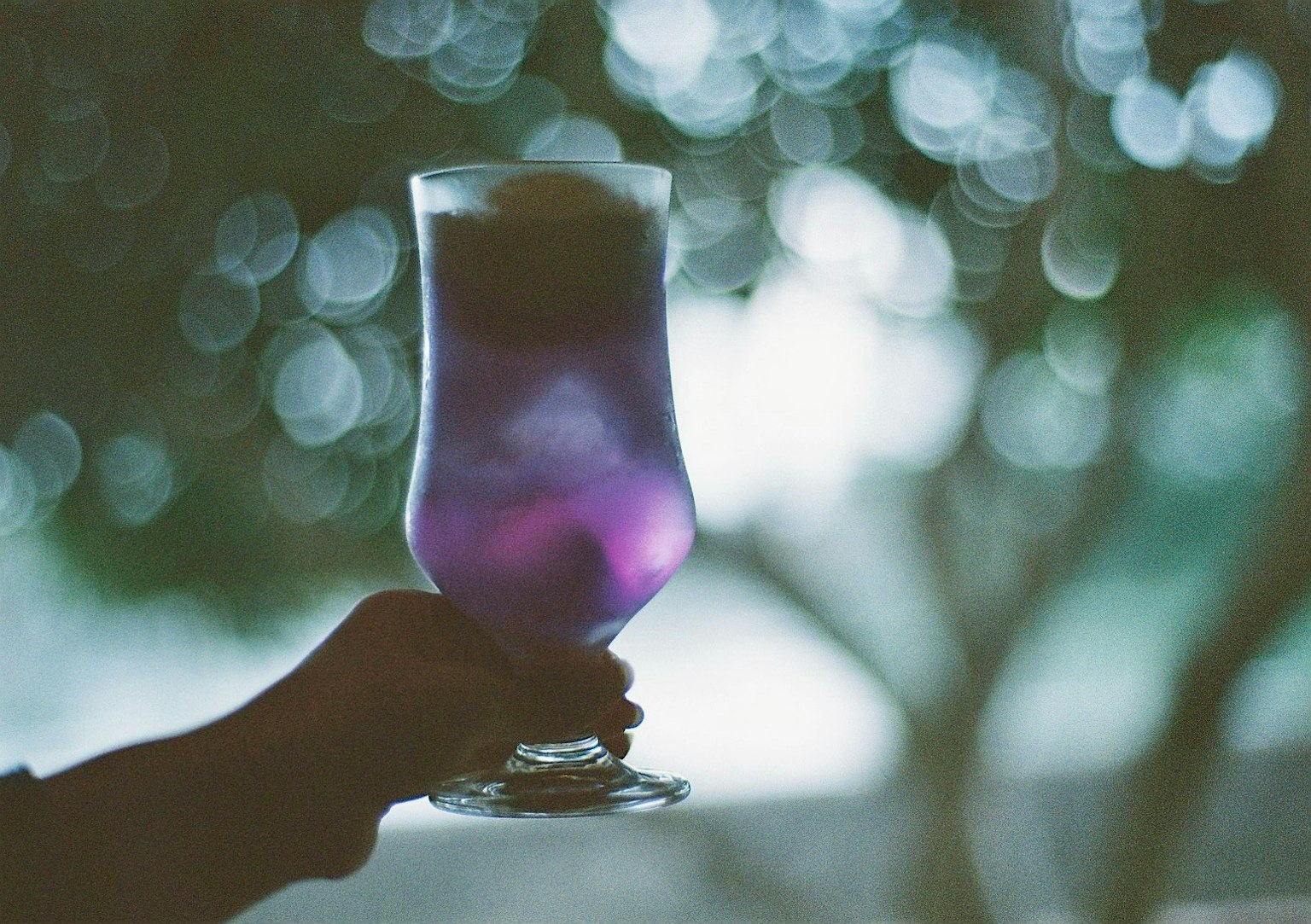 Purple cocktail glass held in hand with a blurred background