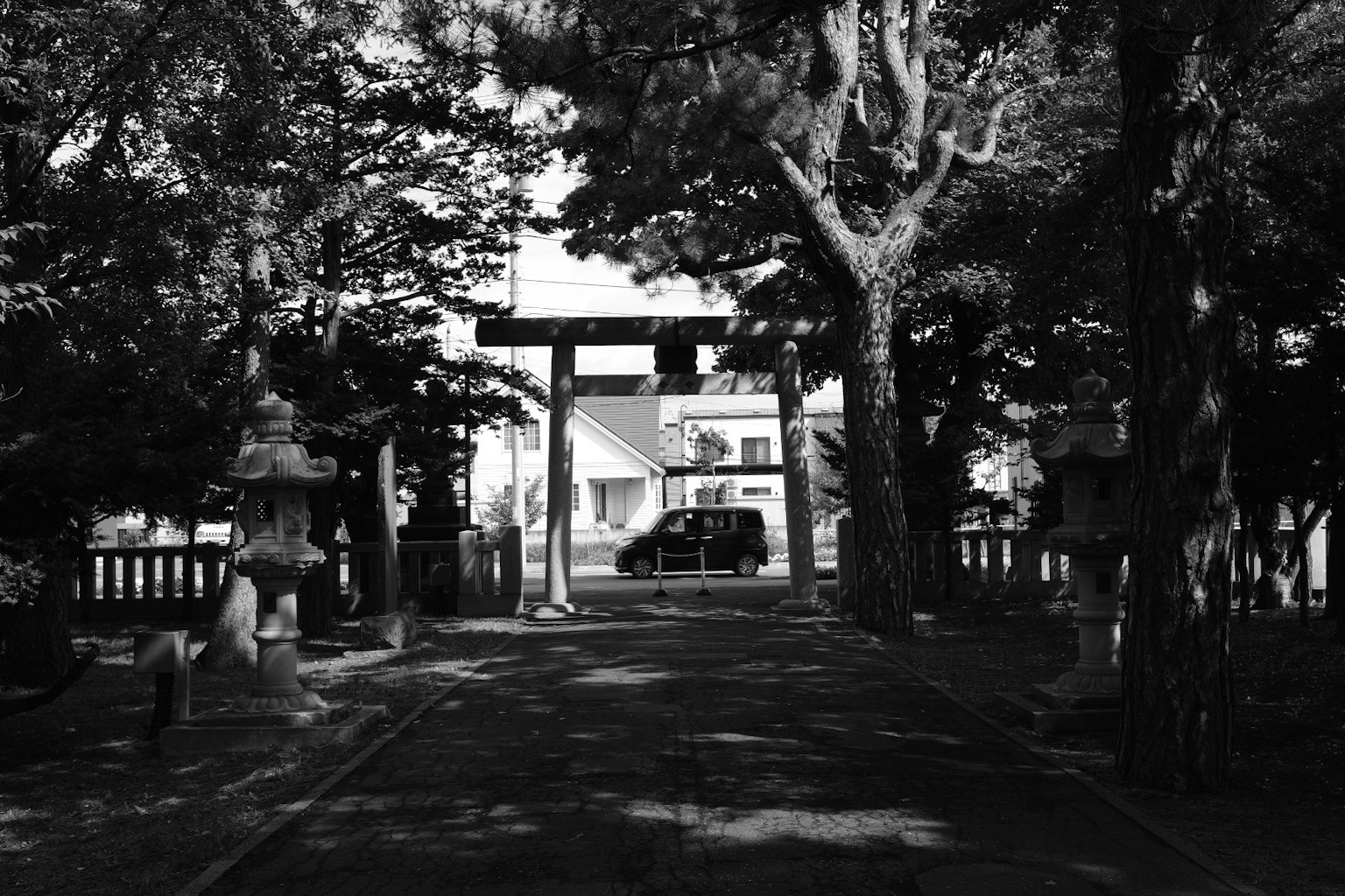 Weg von Bäumen umrahmt mit einem Torii und einem Haus im Hintergrund