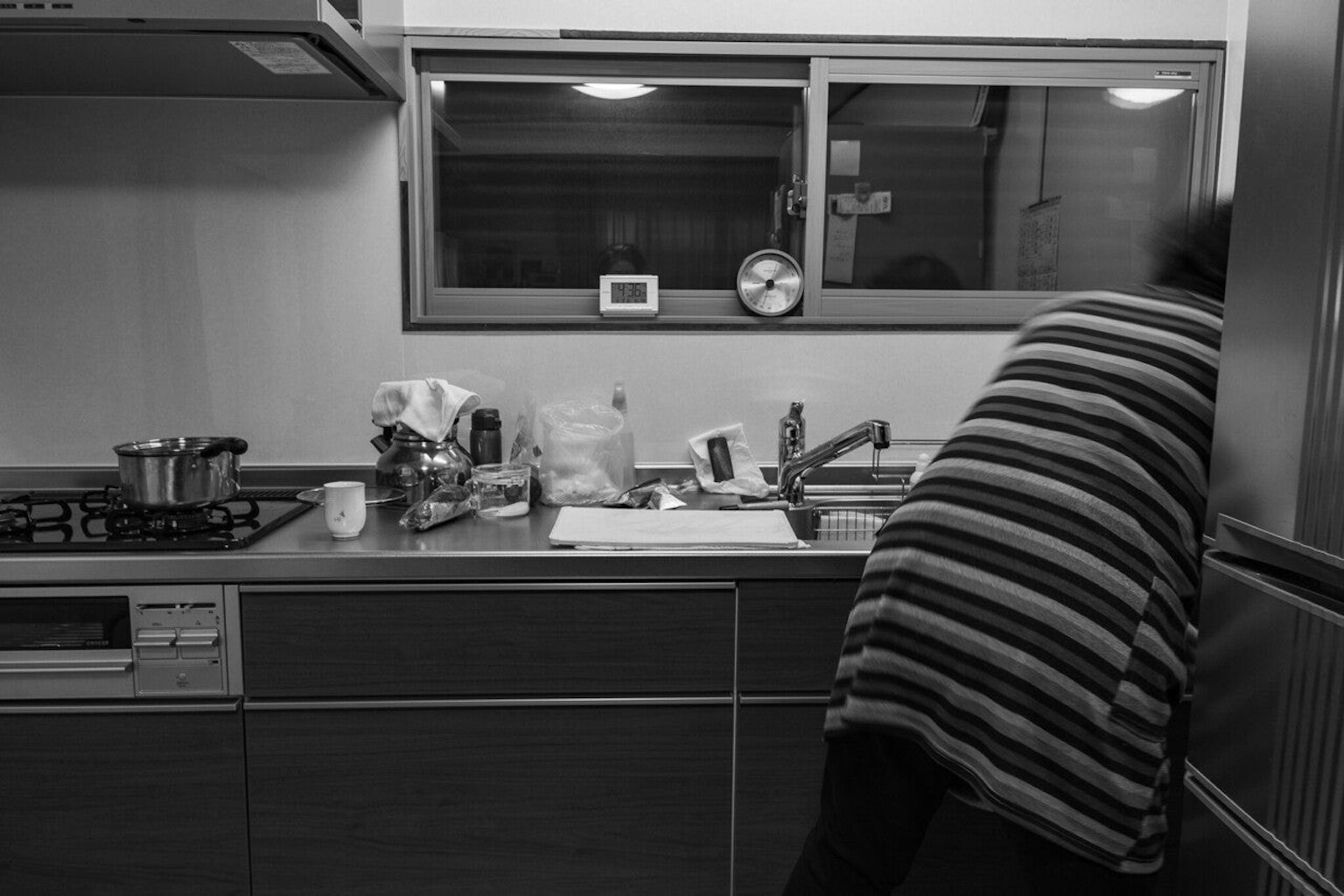 Image en noir et blanc d'une personne faisant la vaisselle dans une cuisine