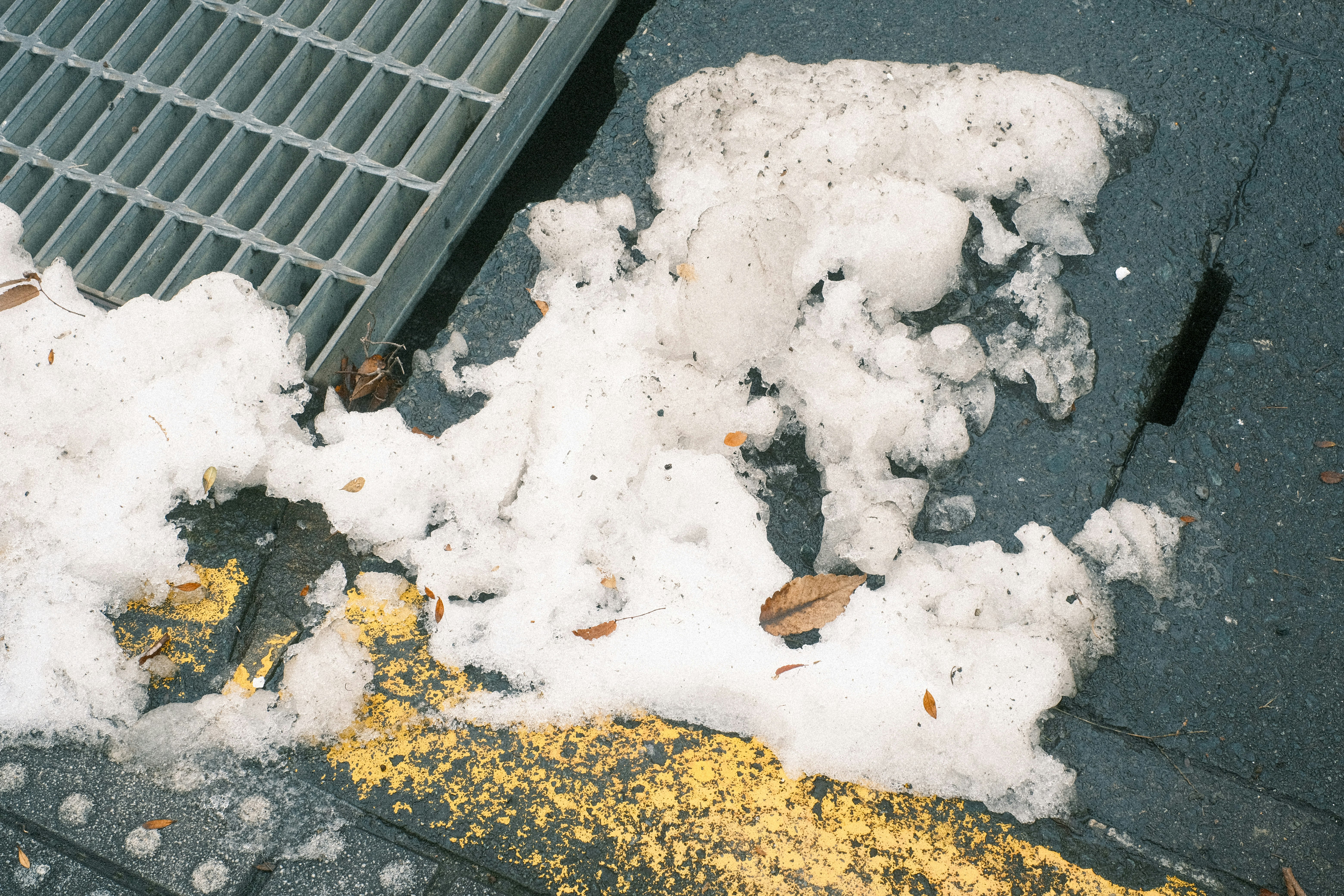 Nieve y hielo acumulados alrededor de una alcantarilla en la acera